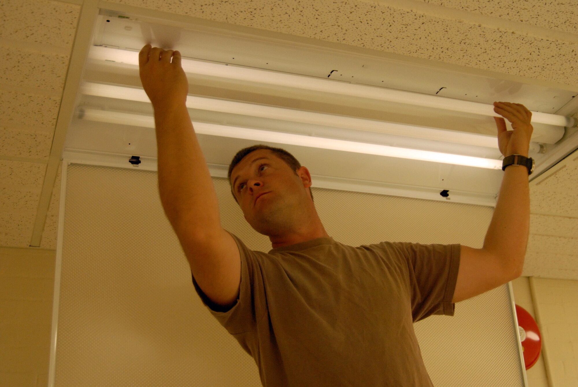Tech. Sgt. Sean Cecil installs fluorescent bulbs into a light fixture for one of the newly renovated classrooms at the Mintos Armory. (Photo by Senior Airman Jason Ketterer, Kentucky Air National Guard.)