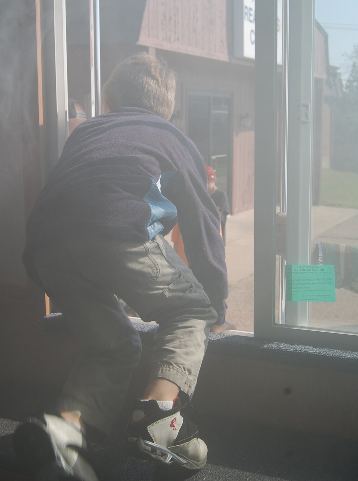 Devin Fox climbs out the window of the smoke house after checking if the bedroom door was hot during a simulated fire.  Devin learned if the bedroom door is hot there may be fire behind it and to find another way out. (Photo by Airman 1st Class Jessica Donnelly)