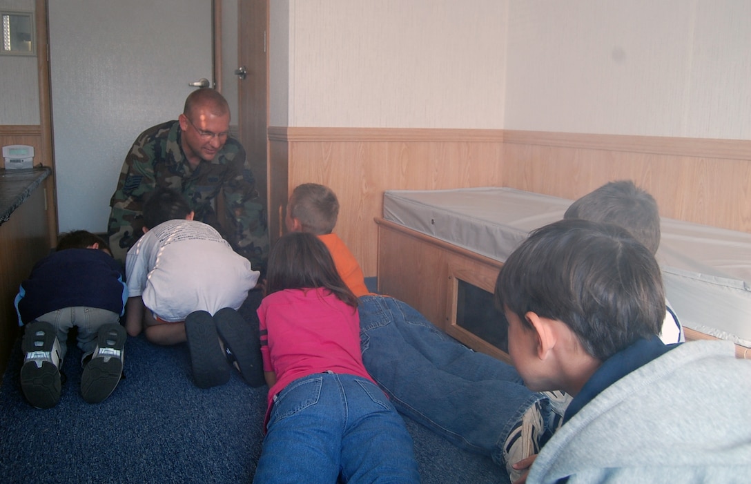 Tech. Sgt. Eric Hartman, 231st Civil Engineering Flight fire protection coordinator, teaches the children from Scooby?s Den to crawl low to the floor as smoke fills the room in a simulated fire.  Sergeant Hartman explained to the children to have two plans of escape in case of a fire. (Photo by Airman 1st Class Jessica Donnelly)