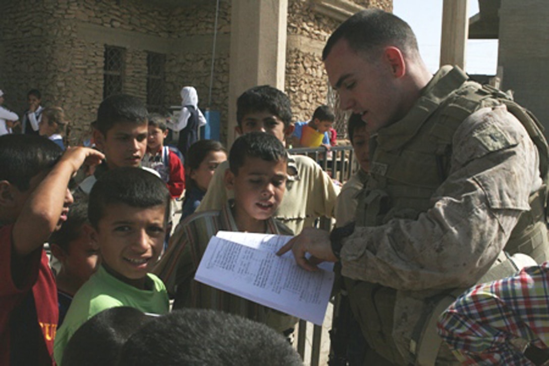 First Lt. Mike Gallagher, an intelligence officer with Task Force 2nd Battalion, 2nd Marine Regiment, Regimental Combat Team 5, reads a book donated to the children of the Al Moaine Elementary School in Rawah, Iraq, Oct. 6. The children received soccer equipment and various school supplies from Rawah's "Friendship City," Towamencin, Pa.