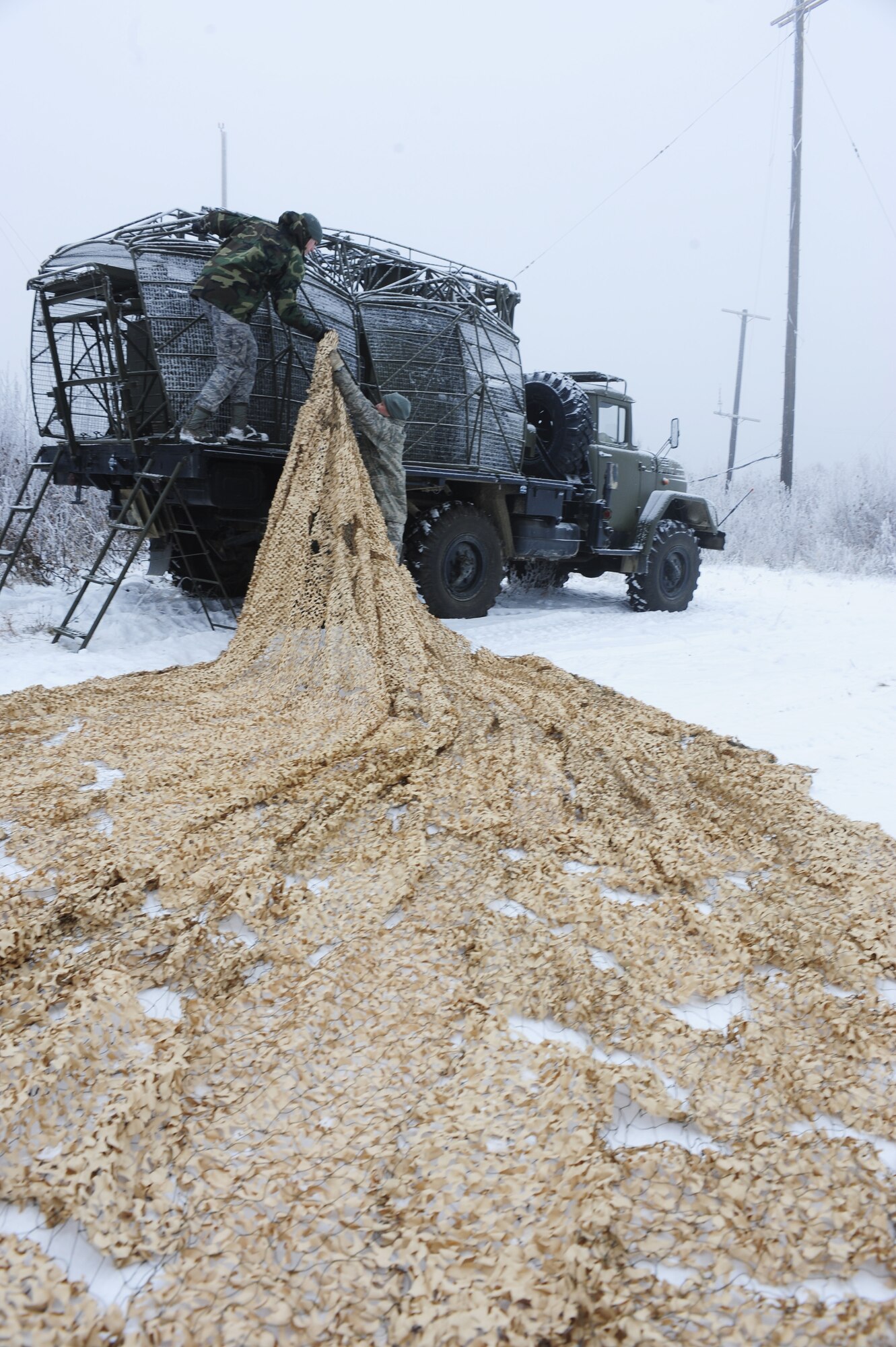 Tech. Sgt. Frank Deans, 353rd Combat Training Squadron, right, hands radar scattering camo netting to Airman 1st Class William Grande, left, as they cover a Russian P-15 flat-face radar truck during RED FLAG-Alaska 09-1 Oct. 6, 2008, at Eielson Air Force Base, Alaska. The 353rd CTS has 25 threats located throughout the Pacific Alaskan Range Complex that emulate a foreign surface to air or anti-aircraft artillery providing threat awareness and intelligence surveillance reconnaissance to the blue forces during exercises.  (U.S. Air Force photo/Airman 1st Class Jonathan Snyder)