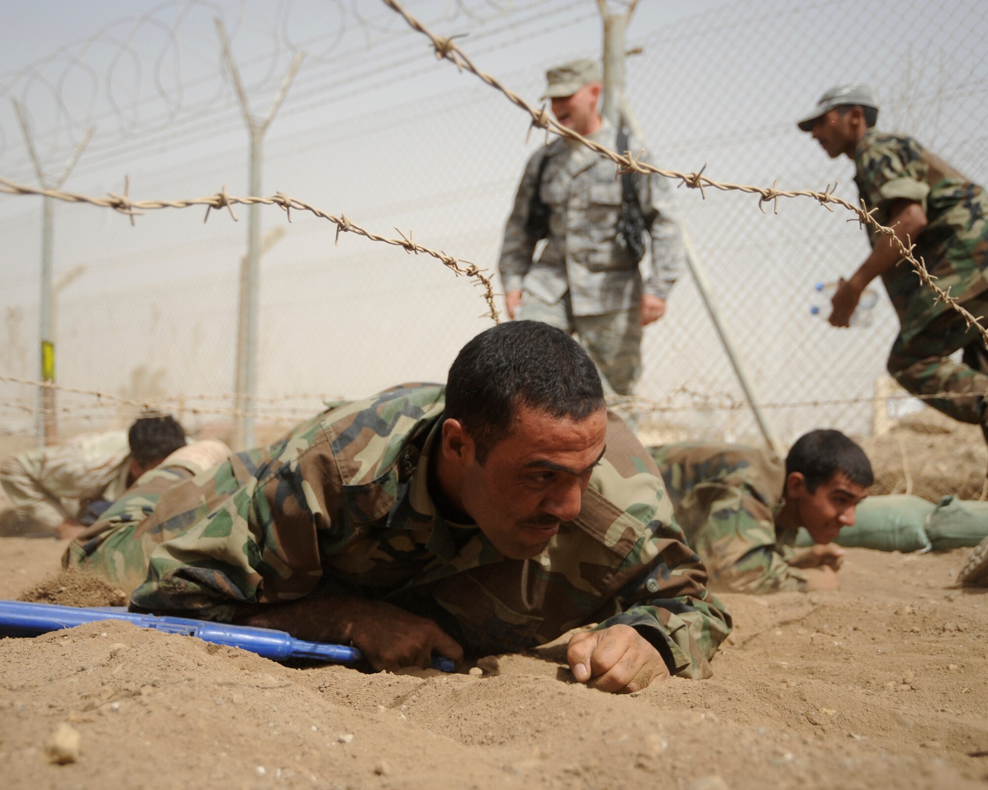 AL TAJI AIR BASE, Iraq -- An Iraqi air force warrant officer low crawls under barbed wire during his run of the  basic military training tactical course while carrying his blue training rifles. (U.S. Air Force photo/Staff Sgt. Paul Villanueva II)