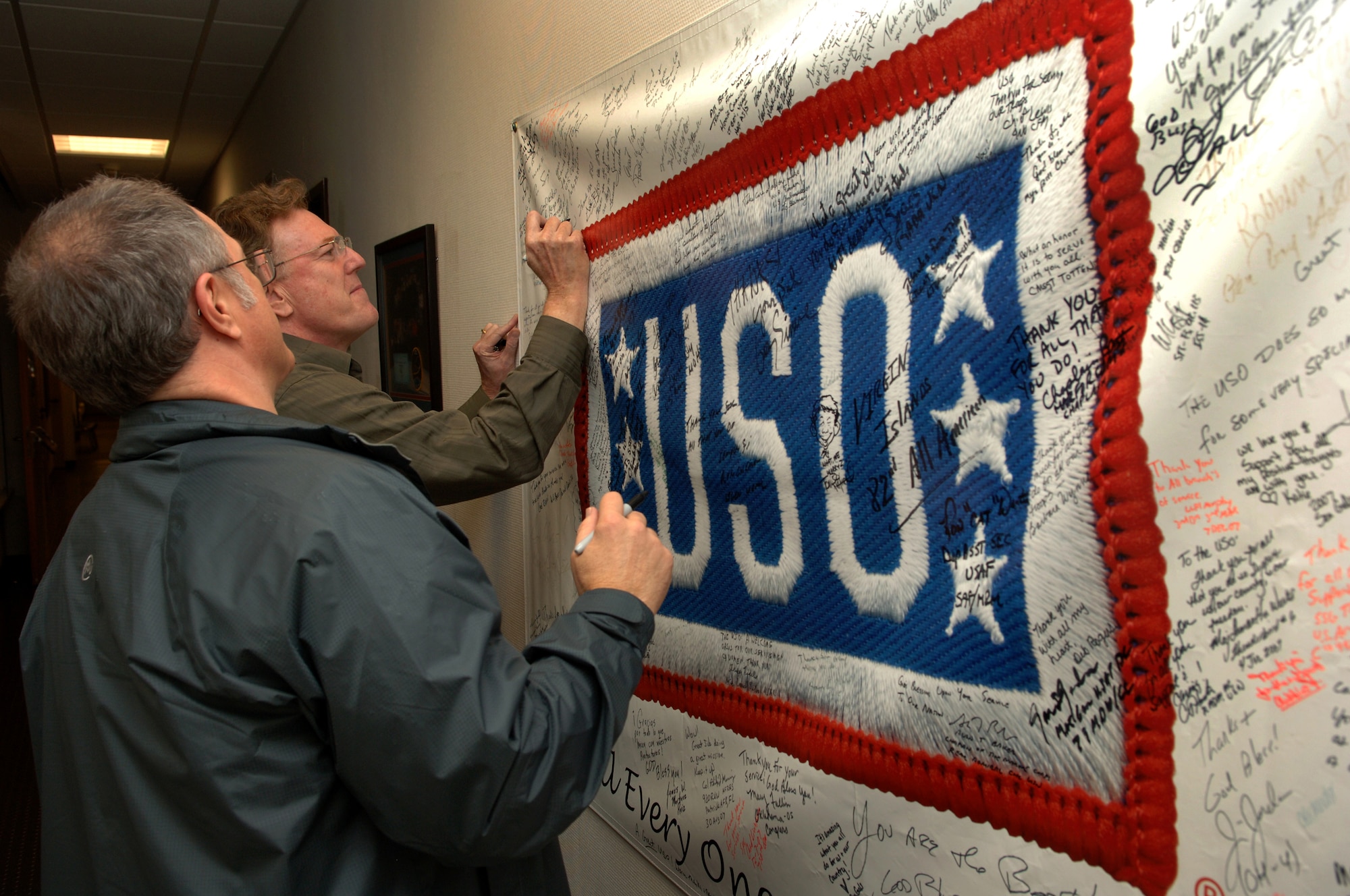 Jeff Keane (left), National Cartoonist Society president  and artist of Family Circus comic strip, and Rick Kirkman, artist of Baby Blues comic strip, signs the USO's distinguished visitors banner at the Contingency Aeromedical Staging Facility, Ramstein Air Base, Germany, Oct. 2, 2008. They are two of eight professional cartoonist from the National Cartoonist Society that visited the CASF as part of a morale tour in cooperation with the USO. (U.S. Air Force photo by Airman 1st Class Tony R. Ritter) (Released)