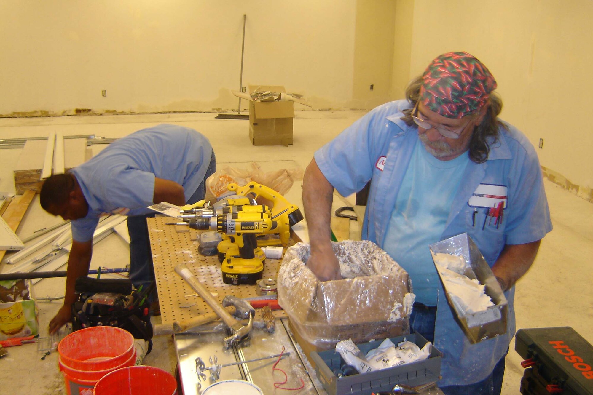 Al Reyna, an AAFES maintenance tech (right), mixes mud he’ll use to texture drywall at the old Class Six location, as Anthony McKoy, AAFES electrician, clears the construction area. (U.S. Air Force photo by Will Alexander)