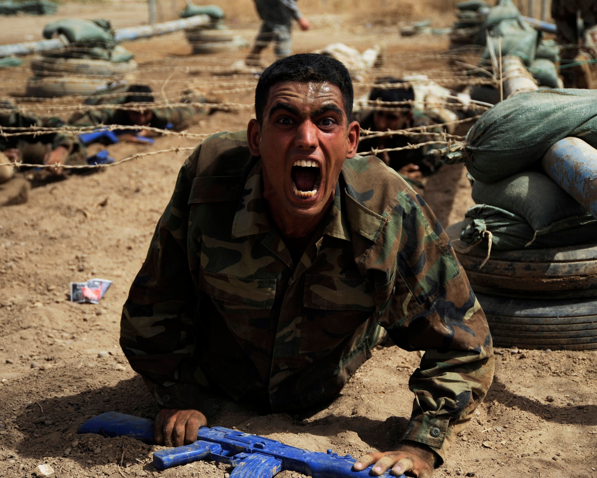 An Iraqi air force warrant officer shows his excitement after low crawling under barbed wire during his run of the basic military training tactical course while carrying his blue training rifle at Al Taji Air Base, Iraq, Sept. 27. (U.S. Air Force photo/Staff Sgt. Paul Villanueva II) 
