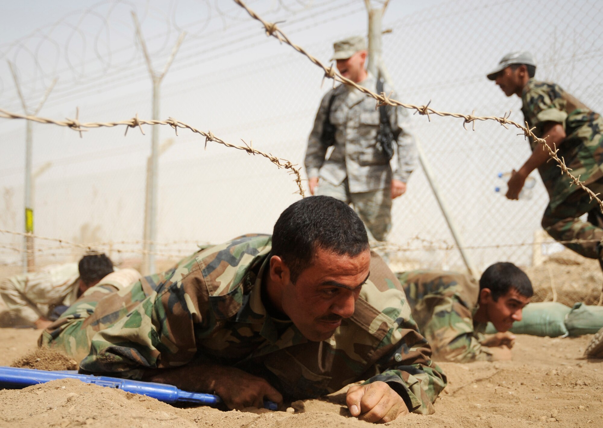 An Iraqi air force warrant officer low crawls under barbed wire during his run of the basic military training tactical course while carrying his blue training rifle. (U.S. Air Force photo/Staff Sgt. Paul Villanueva II) 
