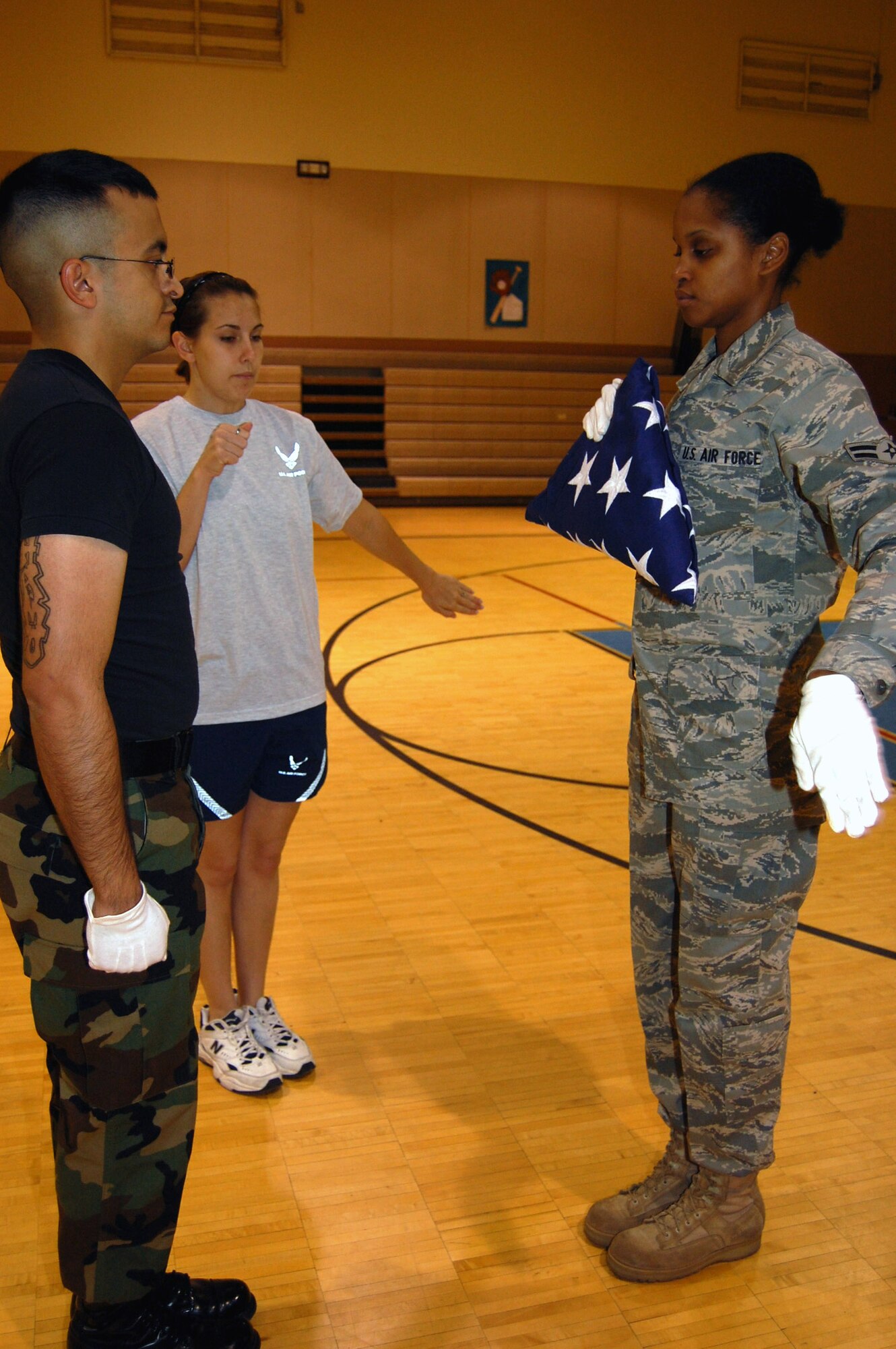 Honor Guard trainers Airman 1st Class Josue Silva, 10th Missile Squadron, and  Airman 1st Class Amber Bratsberg, 341st Logistics Readiness Squadron, teach Airman 1st Class Desiree Gathers how to dress the flag Oct. 3 during a week-long training for 18 new Honor Guard members. (U.S. Air Force photo/Senior Airman Emerald Ralston)
