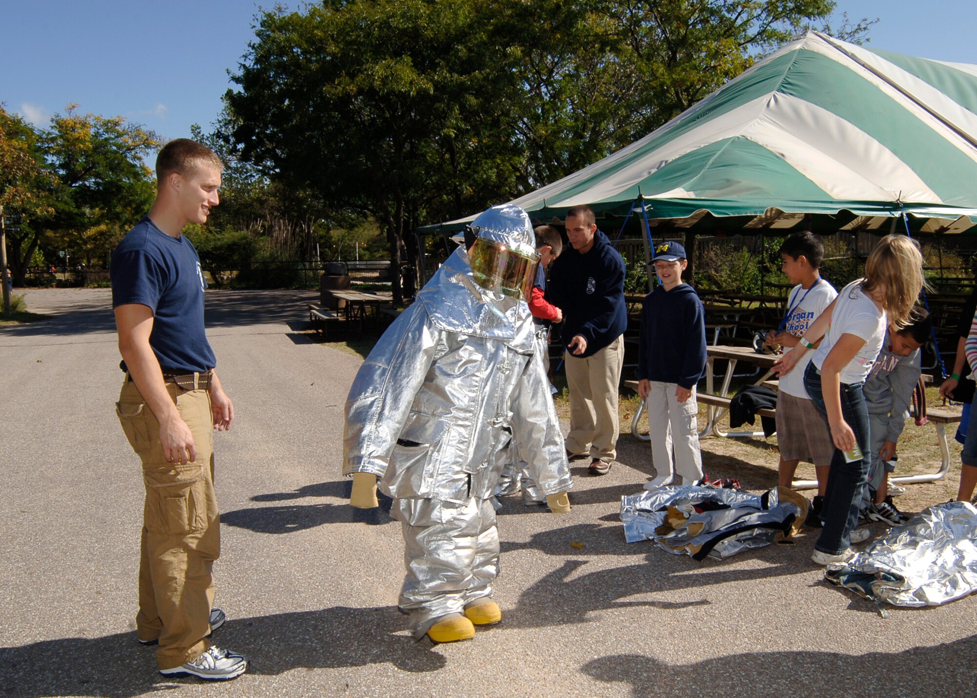 SEDGWICK COUNTY ZOO, Kan. -- Airmen 1st Class Gregory Hoyt and Christopher Vullmahn, 22nd Civil Engineer Squadron fire department, assist fifth-grade pupils from Morgan Elementary in putting on proximity gear, Oct. 7. (Photo by Airman 1st Class Maria Ruiz)