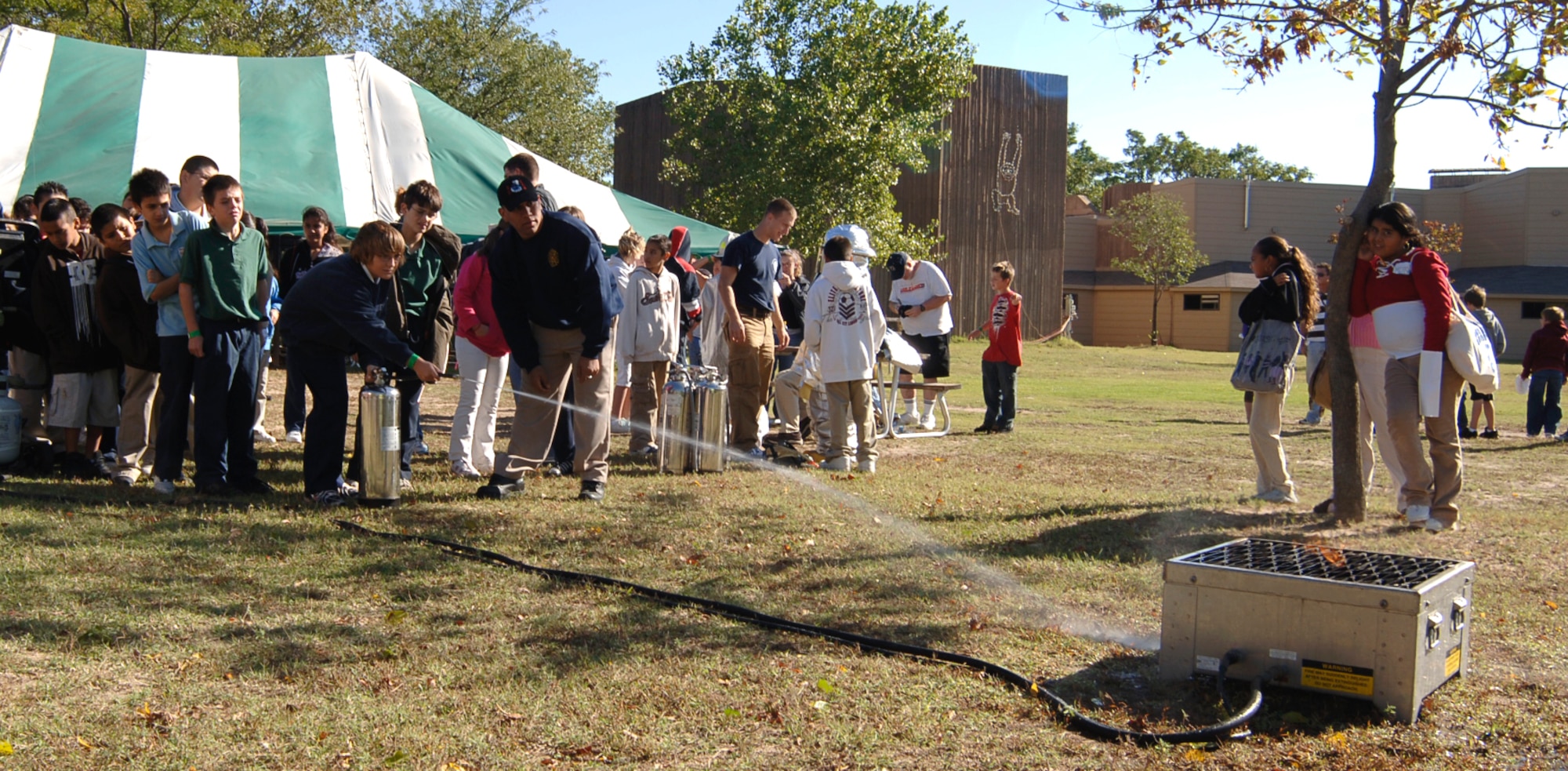 SEDGWICK COUNTY ZOO, Kan. -- Airman 1st Class Juan Ramirez, 22nd Civil Engineer Squadron, helps fifth-grade pupils from Cloud Elementary School put out a fire from a propane extinguisher trainer, Oct. 7. (Photo by Airman 1st Class Maria Ruiz)