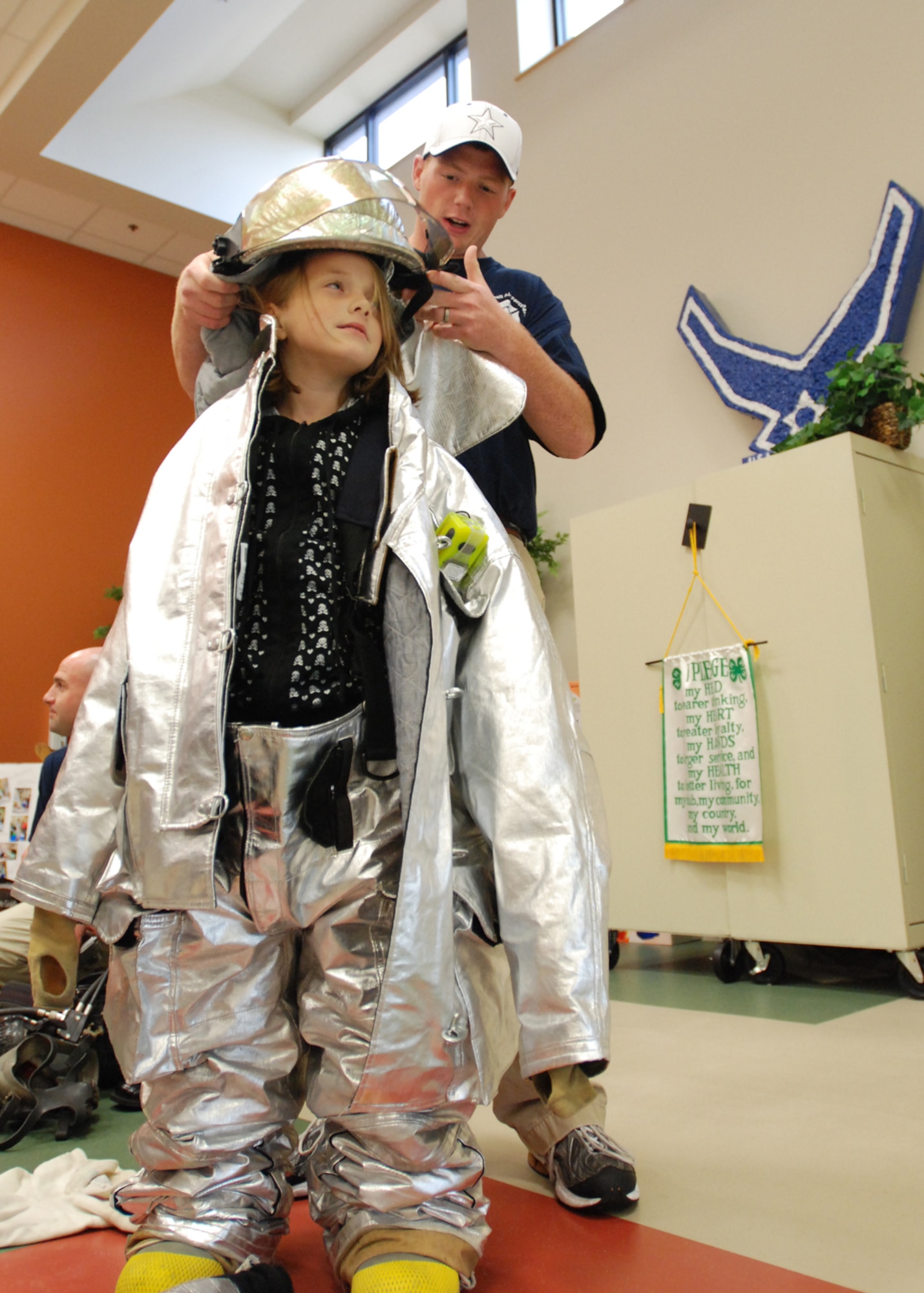 Airman 1st Class William Pritchett, 22nd Air Refueling Wing fireman, dresses Emilee Patten, daughter Tech Sgt. Shawn Patten and wife, Corina, in bunker gear (fire suit) during Fire Prevention Week at the McConnell School Age Program, Oct 6. (Photo by Airman 1st Class Jessica Lockoski)