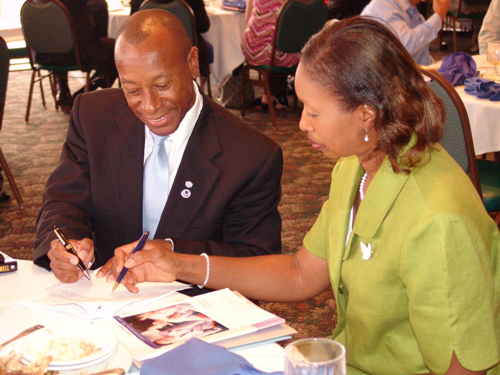 After moving the crowd with inspiring words, Christopher Echols, 96th Communications Group deputy commander signs himself up as a mentor to Glenda Stewart, 96th Mission Support Group plans and programs specialist during the Team Eglin Mentorship Program kick off at the Officers' Club Oct. 9. Mr. Echols compared himself to John Hancock signing the Declaration of Independence during what he called a historical Team Eglin moment. After signing this mentoring agreement of understanding, mentors and mentees will begin to meet regularly and all will attend quarterly luncheons similar to the one for the kick off.