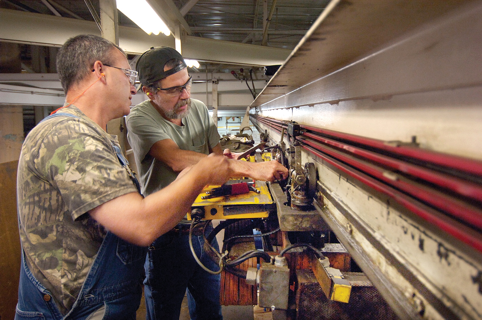 Greg White, front, and Robert Eisenbrey take advantage of the quieter hours of night to repair tools and machines necessary to keep production flowing in Bldg. 3001.  The 76th Maintenance Wing Support Group plant management team work high over the Chemical Cleaning shop to repair a transporter that lifts and moves parts to several vats of cleaners. (Air Force photo/Margo Wright)