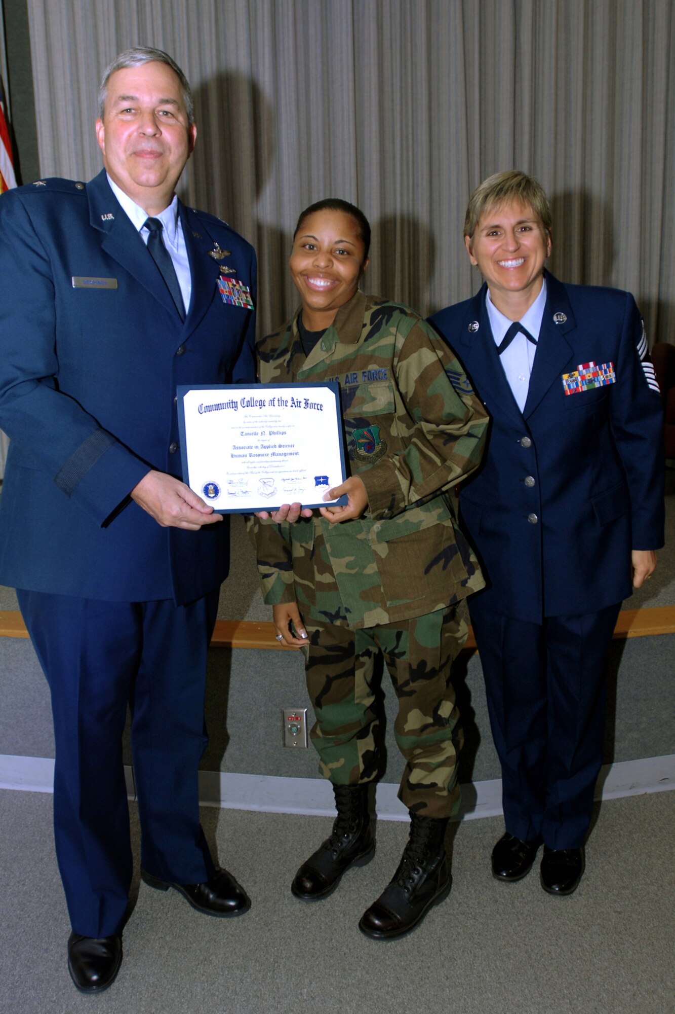 GRISSOM AIR RESERVE BASE, Ind., -- Staff Sgt. Tanielle Phillips, 434th Mission Support Flight career assistance provider, displays her degree in front of a packed audience during a Community College of the Air Force graduation ceremony held here during the October UTA. Sergeant Phillips graduated with a degree in human resources management. Pictured alongside Sergeant Phillips are Brig. Gen. Dean Despinoy, 434th Air Refueling Wing commander, and Chief Master Sergeant Peri Rogowski, 434th ARW command chief. CCAF is the largest community college in the world and is the only community college in the Department of Defense. Each year about 1.6 million semester hours are earned in CCAF classrooms. (U.S. Air Force photo/Staff Sgt. Mark Orders-Woempner)