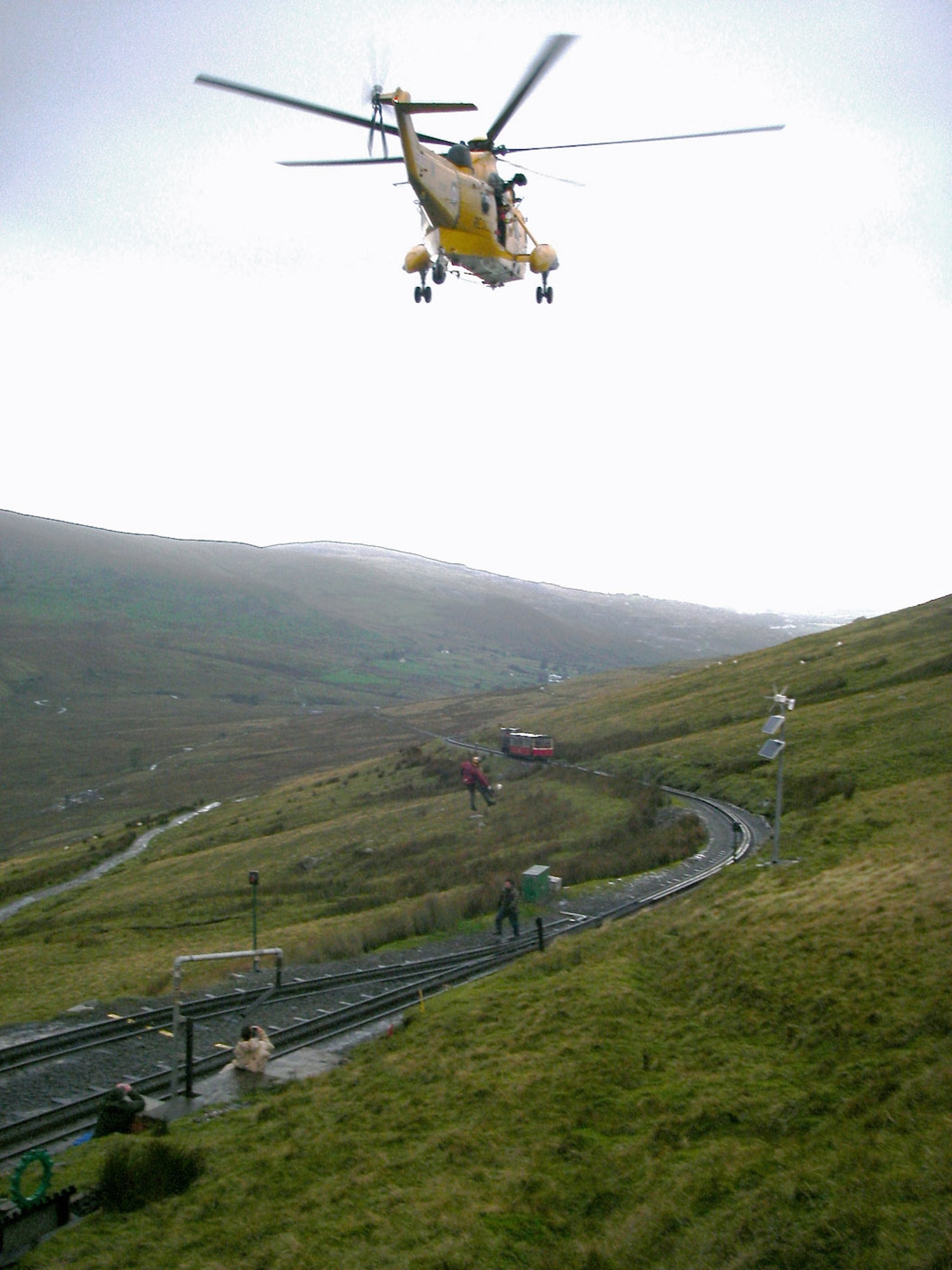 A rescue helicopter from 22 Squadron, Royal Air Force Valley, Wales, winches up the casualty from halfway down Mount Snowdon, ready to take him to the hospital. Three British firefighters, Alan Coldwell, Chris Gould, and Jerry Miles, all 100th Civil Engineer Squadron fire department, and their mountain guide, Dave Wainwright, 100th Force Support Squadron outdoor recreation, rescued the man they found alone and suffering from hypothermia and frostbite at the peak of Mount Snowdon Oct. 3. After calling emergency services, the four helped bring him halfway down the mountain, with the help of passengers on a train from Snowdon Mountain Railway. The train never usually runs at this time of the year as the weather is too bad, but by coincidence, it was taking passengers to the top of Mount Snowdon at the same time the firefighters found the man. (Courtesy photo/Doug Blair, Snowdon Mountain Railway)
