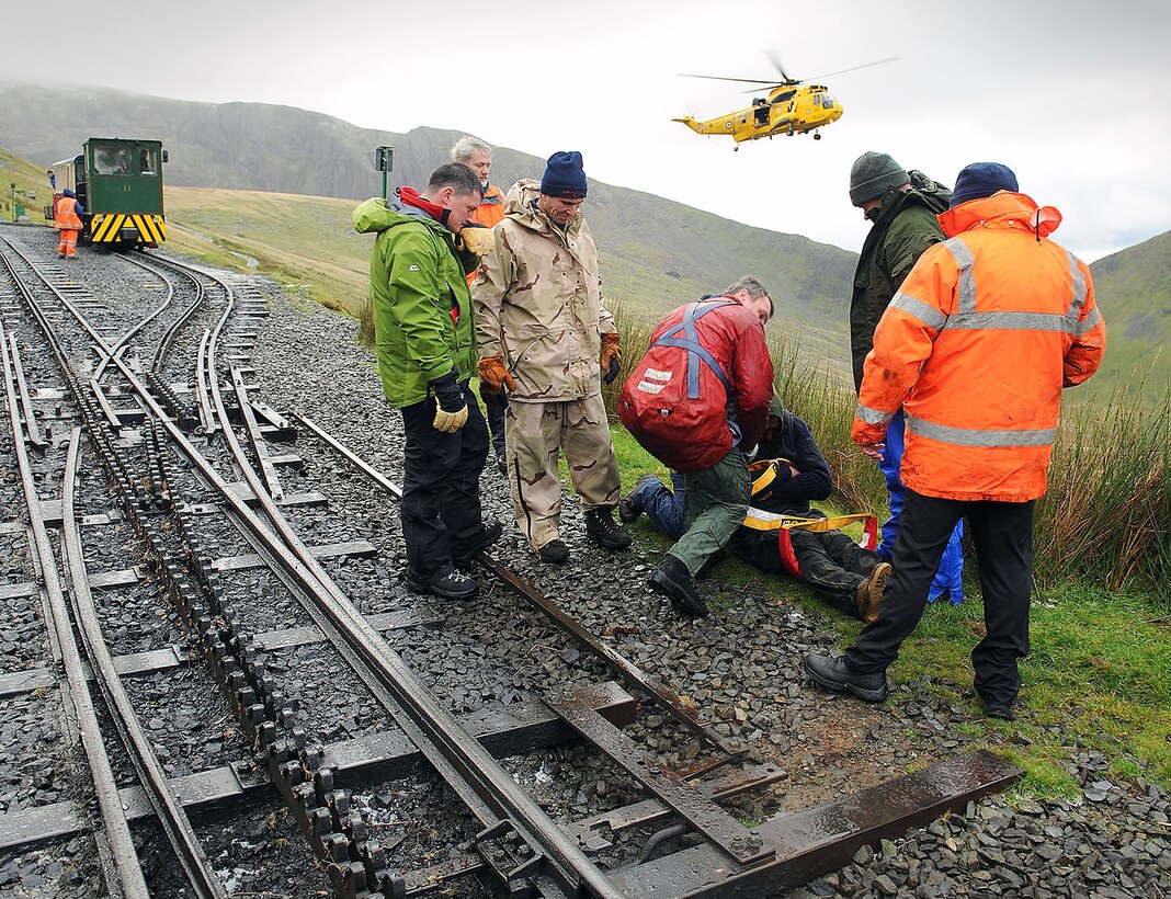 Dave Wainwright, Chris Gould, Jerry Myles and Alan Coldwell watch with members of the Snowdon Mountain Railway to ensure the casualty they rescued from the top of Mount Snowdon is safely prepared by the winchman to be taken up into the rescue helicopter from 22 Squadron, Royal Air Force Valley, Wales. Mr. Wainwright is the 100th Force Support Squadron outdoor recreation director. Mr. Gould, Myles and Coldwell are Defence Fire Service firefighters assigned to the 100th Civil Engineer Squadron. (Courtesy photo/Snowdon Mountain Railway)