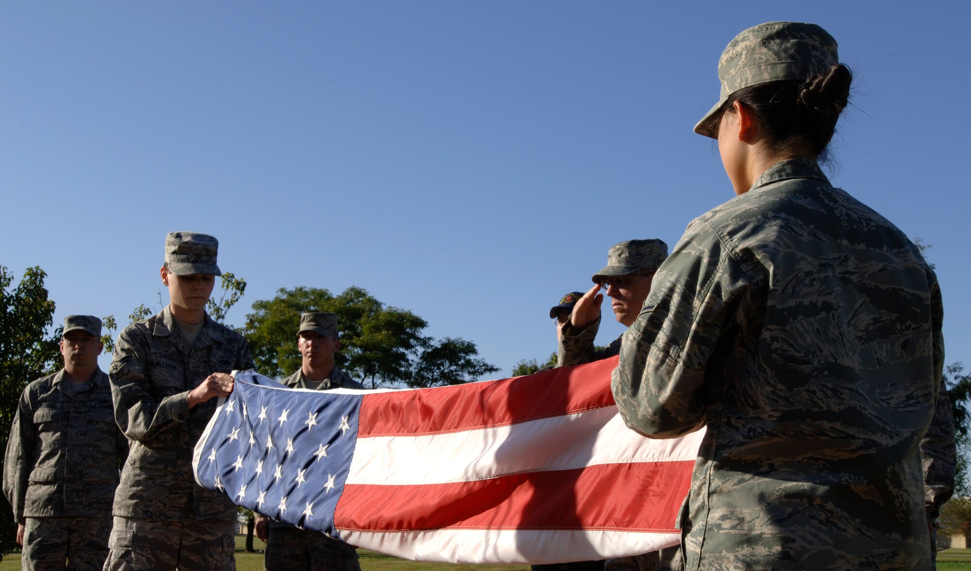 MCCONNELL AIR FORCE BASE, Kan. -- Airman 1st Class Michael Furlogh, Tech. Sgt. Michael Davis, and Airman San Choe, 22nd Maintenance Operations Squadron, fold the American flag during a retreat ceremony held outside the wing headquarters building, Oct. 2. The flag folding ceremony is a tradition in the Air Force signifying the end of a duty day, even in a 24-hour operations area. (Photo by Senior Airman Laura Suttles)