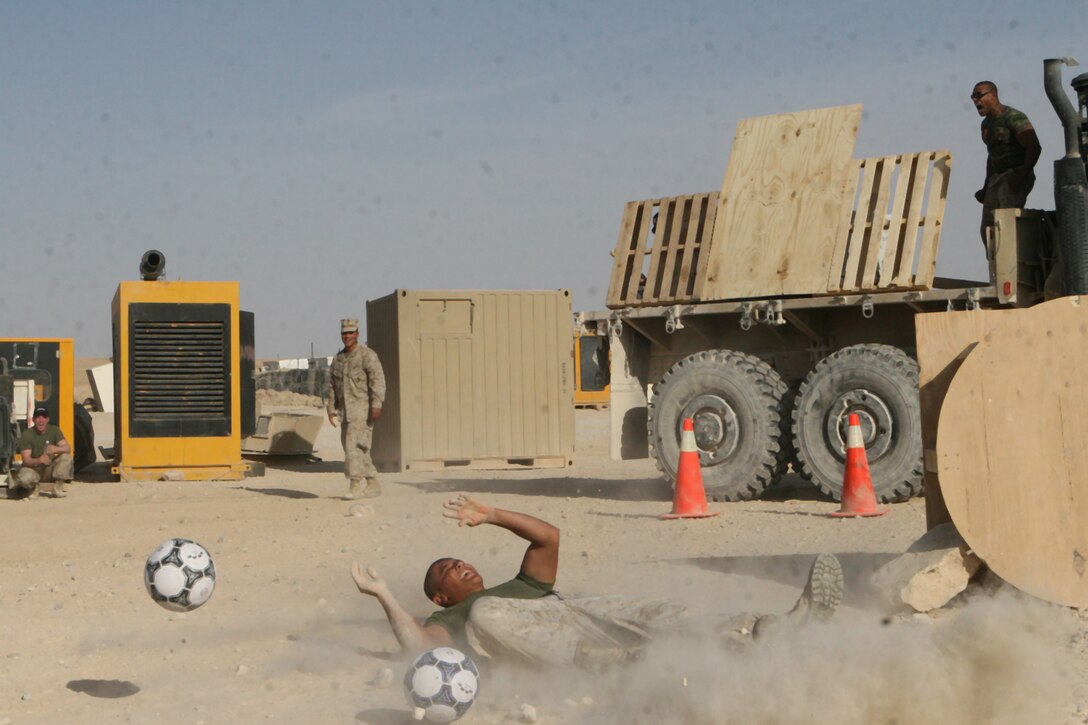 Cpl. Trevor Ryan, a small arms repairer/technician with Task Force 2nd Battalion, 2nd Marine Regiment, Regimental Combat Team 5, slides across the dirt after a barrage of soccer balls landed on target at Combat Outpost Rawah, Iraq, Oct. 9. Militia, a gladiator from the TV series â??American Gladiators,â? bellows in victory, trying to drown out the cheers of the nearby crowd.  Titan, Phoenix, Militia, Venom and Panther came to meet the service members on the outpost and play the Marine Corps variation of the â??Assault Courseâ? event from the series.