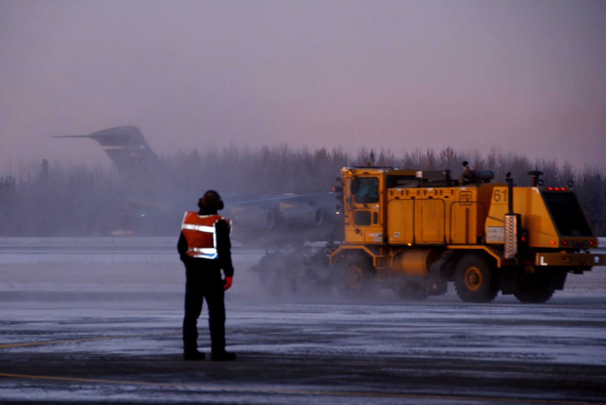 A crew chief waits to guide a C-17 Globemaster III Oct. 9, 2008 at Eielson Air Force Base, Alaska. A small emplacement excavator snow plow removes snow from the run way to ensure flying operations are always "Ready to go at 50 below". (U.S. Air Force photo by Airman Laura Max)