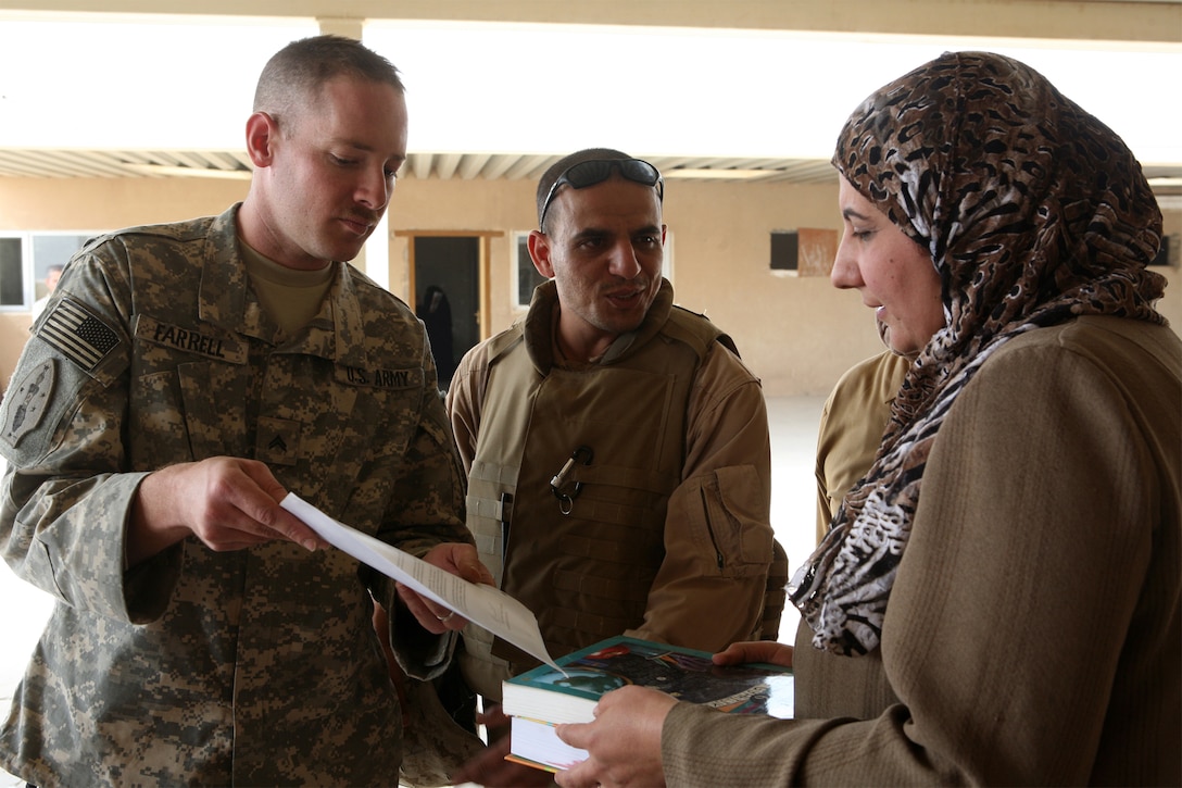 Army Cpl. Greg Farrell, an assistant team leader from Denver, attached to Task Force 1st Battalion, 2nd Marine Regiment Regimental Combat Team 1, presents text books to an Iraqi school teacher, recently. School supplies were donated to the Tri-Cities area schools by the Southeast Denver Rotary Club.