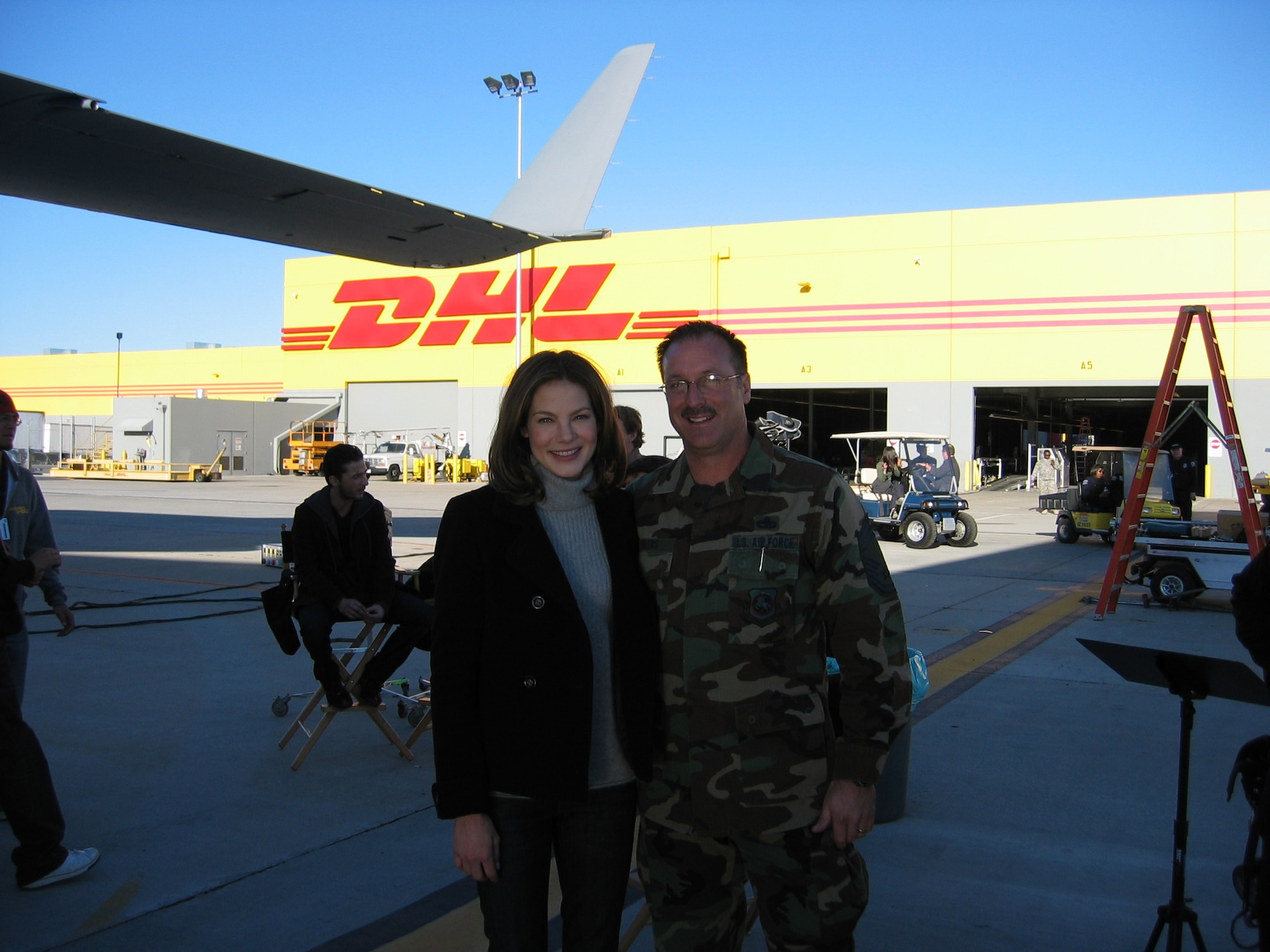 Chief Master Sgt. Robert Ehlers, 56 APS, poses with Michelle Monaghan on the set of "Eagle Eye." Actor Shia LaBeouf (left), awaits the next scene. More than 30 members from March participated in last weekend’s box office hit “Eagle Eye” during its filming at March ARB. Airmen, Soldiers, civilian employees and employees at the DHL distribution center at the south end of the base were all involved in various scenes. The DHL hub was used for a chase scene where the actors slid down and crawled across equipment, while military members participated as extras, posing as TSA and airport police. A C-17 aircraft was also featured. In the movie, LaBeouf and co-star Monaghan are strangers thrown together in dangerous situations after they receive a phone call by a mysterious woman who threatens their lives and their families. Throughout their travels, they are watched through everyday technology and are eventually marked as terrorists who become the most wanted people in the country. (U.S. Air Force photo) 