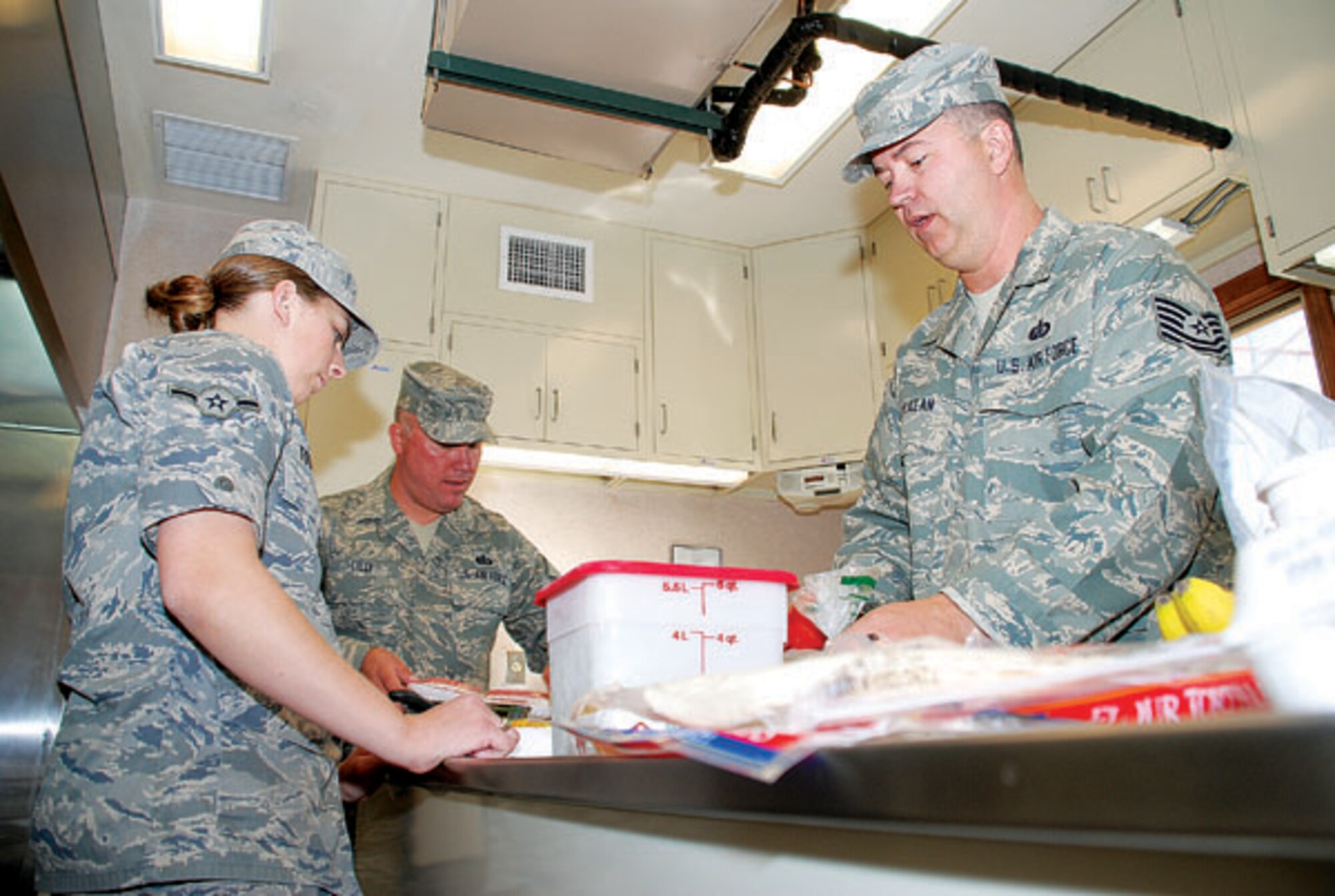 Airman Elizabeth Touhey, 319th Missile Squadron chef, watches Master Sgt. Patrick Lilly and Tech. Sgt. Charles McKean, Air Force Space Command CCommander Gen. C. Robert Kehler's enlisted aides, prepare to cook food Sept. 24. (Photo by 2nd Lt. Brooke Brzozowske)
