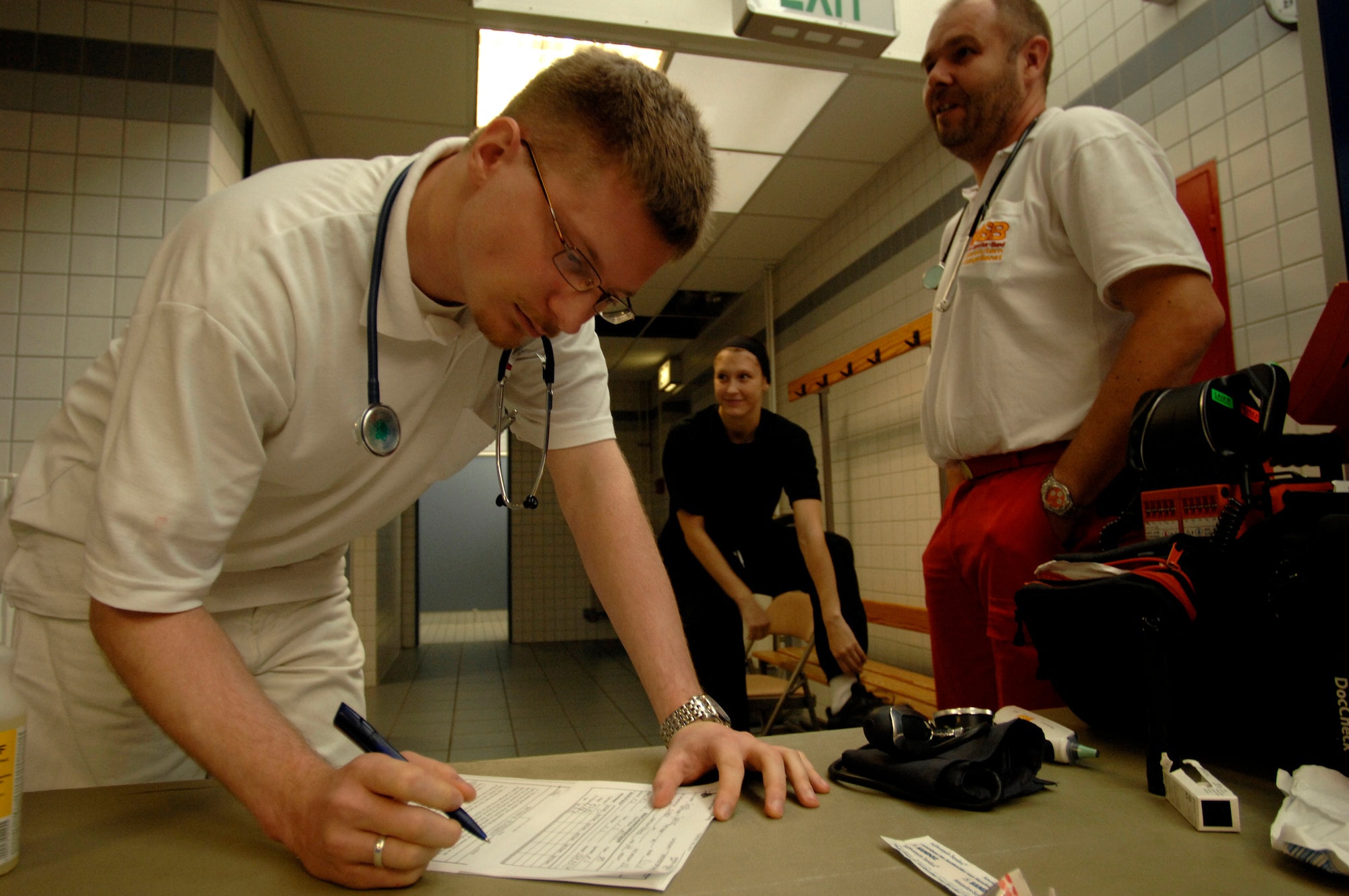 Dr. Wolfgang Hoffmann (left) and Thomas Weilemann emergency medical technician(right), both from the Arbeiter ? Samariter-Bund (ASB), Kaiserslautern, reviews paper for German female boxer Janine Gertel from the Turngemeinde Worms Boxing Club prior to her match, Vogelweh Air Base, Germany, Oct. 11, 2008. Gertel was the only female boxer that registered to compete allowing her to win the gold medal by default. (U.S. Air Force photo by Senior Airman Amber Bressler)(Released)