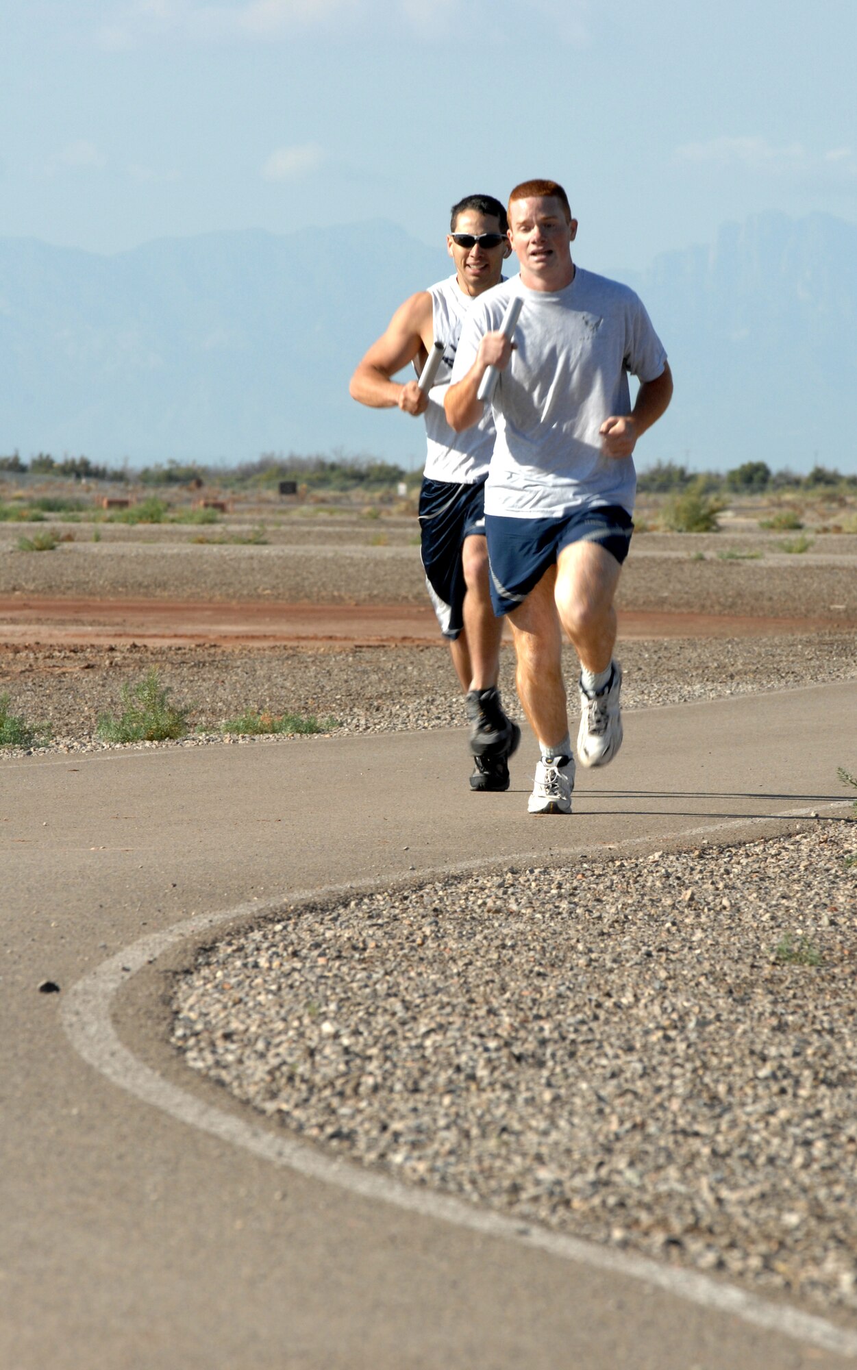 Two participants from the large squadron category run neck-in-neck in the three-mile relay on Sports Day at Holloman Air Force Base, N.M., October 10. The Fitness and Sports Center held 15 events and over 2000 Team Holloman members participated in the event. (U.S. Air Force photo/Airman Sondra M. Escutia)