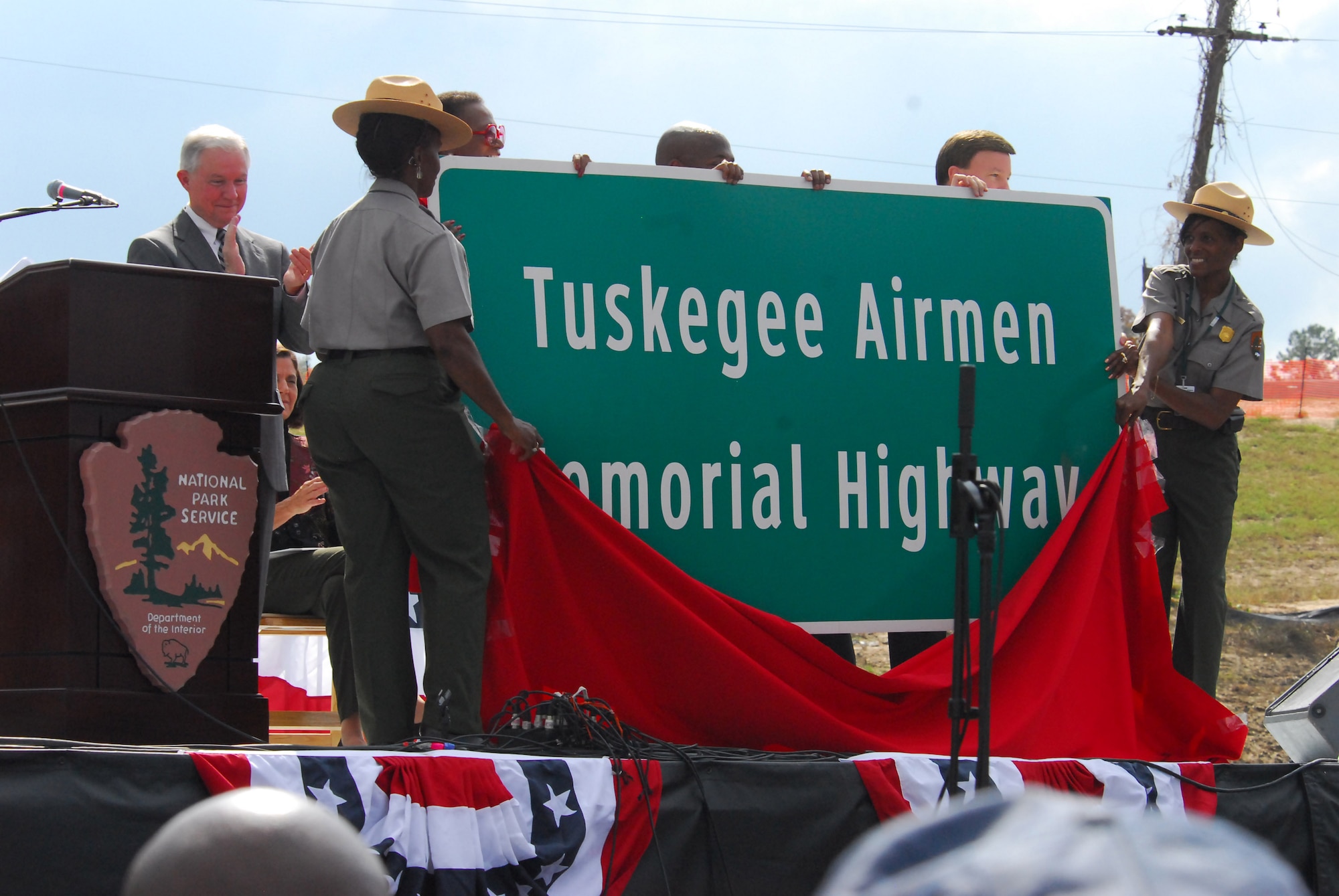 As part of the opening ceremony of the Tuskegee Airmen National Historic Site Oct. 10 at Moton Field, Ala., National Park Service officials unveil a sign that designates part of Interstate 85, which passes near the city of Tuskegee, as the Tuskegee Airmen Memorial Highway. Sen. Jeff Sessions of Alabama looks on from behind. (Air Force photo by Scott Knuteson)