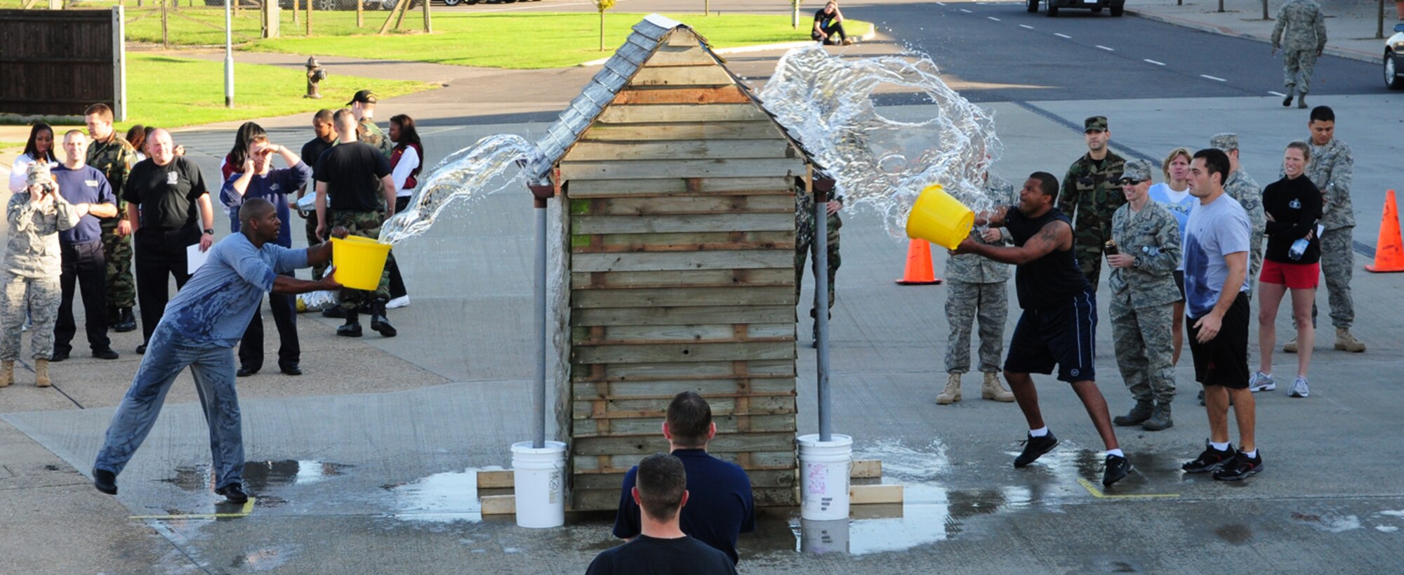 A member of the 100th Civil Engineer Squadron Electrons, left with bucket, and 100th Maintenance Squadron, right with bucket, go head-to-head in the tiebreaker at the fire muster Oct. 9 at the 100th CES Fire Department. The two teams drew in the team event, both gaining a time of 1:54 minutes, so faced each other in an extra event to decide the winner. Team members had to take turns and grab a bucket, fill it with water from a special pool, run to the wooden shed and throw the water onto the roof. It then dripped down the drainpipe and into another container. Whoever filled the white container to overflowing, won. After a hard effort, 100th MXS took the trophy. (U.S. Air Force photo by Karen Abeyasekere)