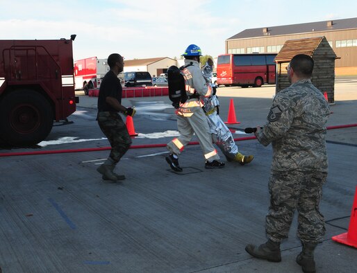 Senior Airman David Norris, center, 100th Civil Engineer Squadron Readiness and Emergency Management, drags a mannequin back towards the finish line at the fire muster Oct. 9, as Staff Sgt. Travis Girley, a firefighter at the 100th CES Fire Department, backs up behind him, ready to catch him if he stumbles. (U.S. Air Force photo by Karen Abeyasekere)