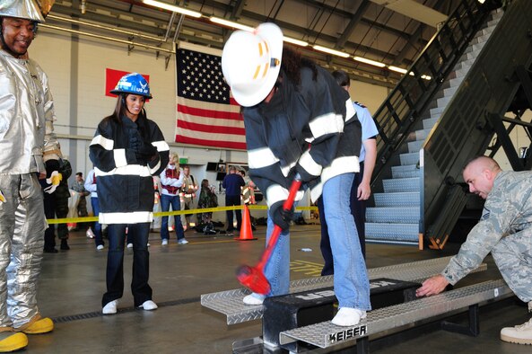 Tequia Hicks, one of the Washington Redskins cheerleaders, tries to hit the sled with a mallet during the team category of the fire muster as fellow cheerleader, Michelle Brandon, cheers her on and Master Sgt. Jim Wenger, right, 100th CES Fire Department, pulls the sled back to help. Staff Sgt. Travis Girley, left, 100th CES firefighter, stands by ready to take over. The event, held Oct. 9, was part of Fire Prevention Week activities which also included demonstrations, and visits by Sparky the Fire Dog to the child development center and a local nursery in Beck Row. The fire department also had an open house Oct. 11 to round off the week. (U.S. Air Force photo by Karen Abeyasekere)