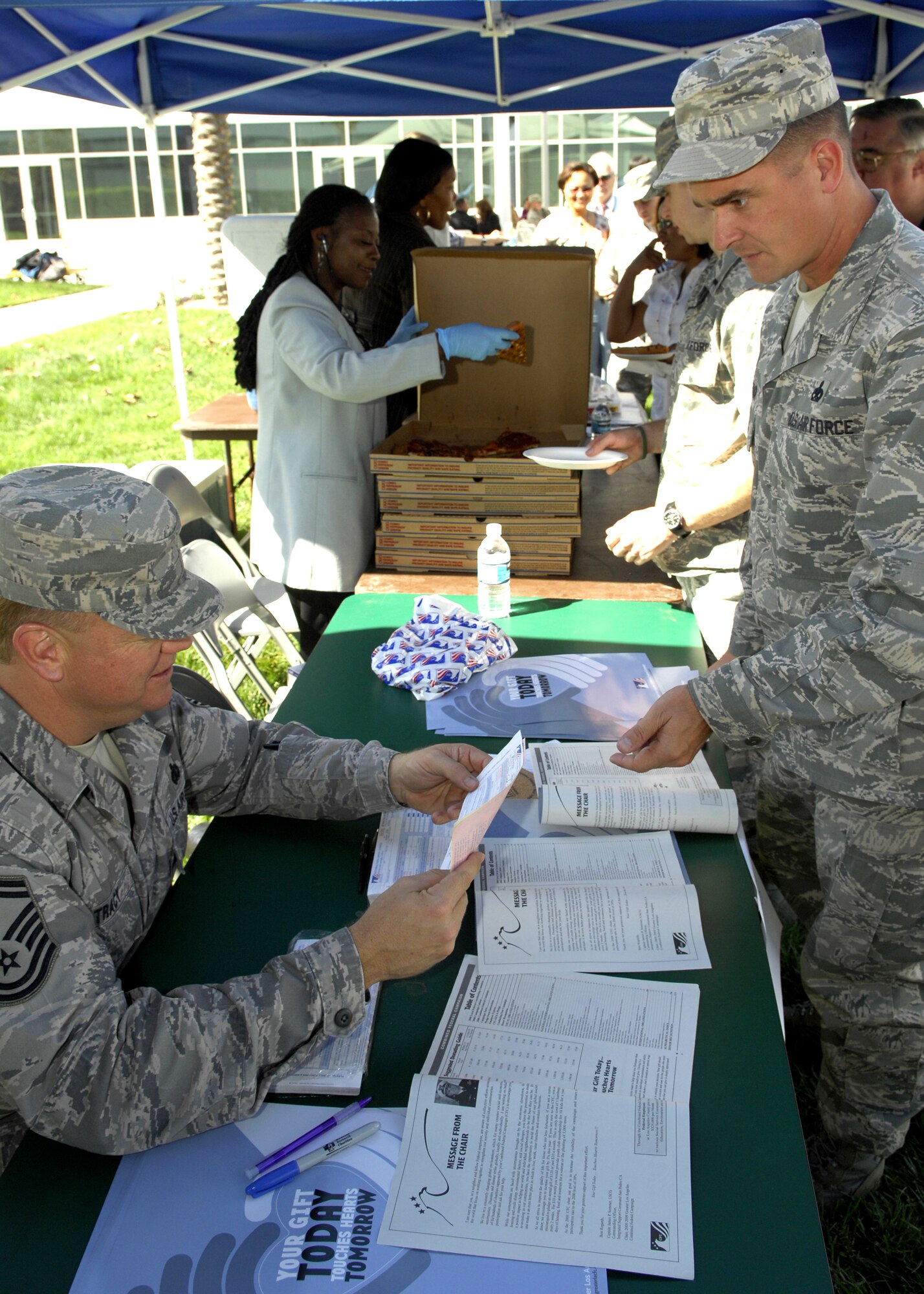 Senior Master Sgt. Douglas Tracy volunteers his time as he reviews the contribution form from Master Sgt. Thomas Raupach, 61st Medical Group, during the Combined Federal Campaign kickoff in the Schriever Space Complex courtyard, Oct. 15.  In the background, base personnel were treated to free pizza and water.  Charitable organizations such as the American Heart Association, American Cancer Association, USO, Big Brothers/Big Sisters, Salvation Army, AIDS ReSearch Alliance, Meals on Wheels West, City of Hope, Mission to Children, the United Way, and others passed out information to attendees.  (Photo by Stephen Schester)