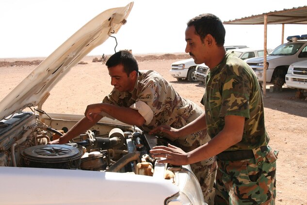 Hamad Yasin Taba (right), 26, teaches one of his Iraqi border patrol counterparts how to perform preventative maintenance on one of the unit's vehicles Oct. 16.  Capitalizing on his classroom time with Staff. Sgt. Marty Vickery, the maintenance chief for the Marine Corps Border Transition Team at Trebil, Iraq, Taba instructed his peers one-on-one.  With his hands and arms covered in engine grease, Taba went through steps and explained the importance of performing these checks to his peers.::r::::n::