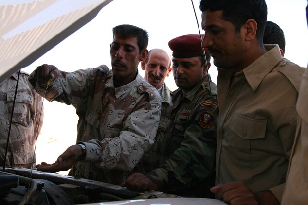 An Iraqi Desert Wolf mechanic at Border Fort 14A along the Jordanian border shows his teammates how to check fluid levels in their vehicle engines Oct. 16.  The border fort was constructed in 2004 to provide a launching pad for Iraqi Security Forces to conduct anti-insurgency and anti-smuggling operations in the country's border.  Marines from the Border Transition Team based at Trebil mentor the Iraqis on a broad range of operational skills.::r::::n::