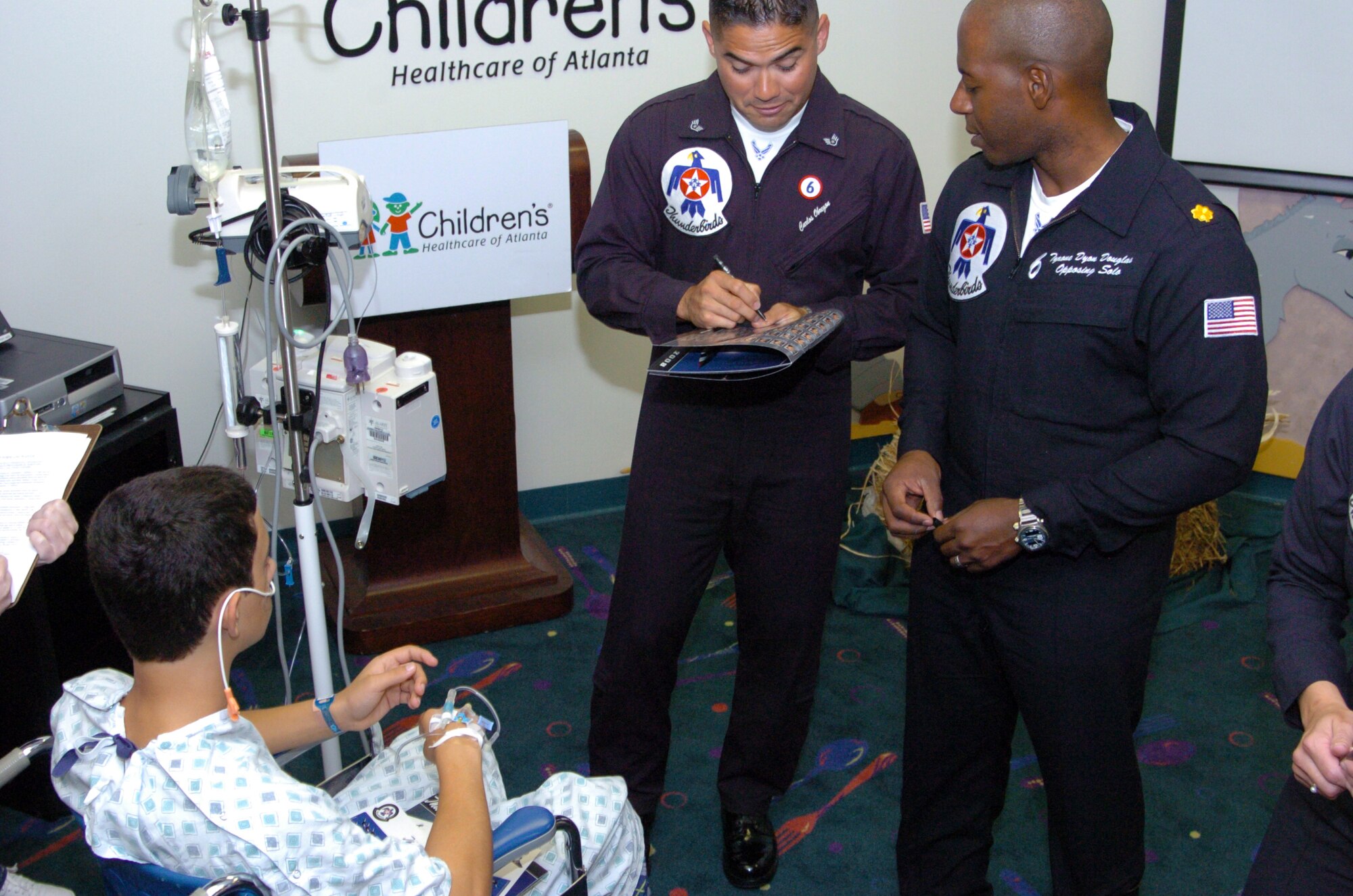 The U.S. Air Force Demonstration Squadron, the Thunderbirds,team members Staff Sgt. Carlos Obregon , assistant crew chief and Maj. Tyrone Douglas, No. 6 F-16 pilot autograph a Thunderbirds' 2008 program book for  Cody Villafranca, 15,  at Children's Healthcare of Atlanta Pediatric Hospital. "We enjoy seeing the smiles on youth's faces when we're able to visit them in the community," said Sergeant Obregon. Thunderbird team members also visited two metro Atlanta High Schools as part of their community relations visits in connection with their appearance at the Wings over Marietta Air Show and Open House at Dobbins ARB, Oct. 18-19. (U.S. Air Force photo/Master Sgt. Stan Coleman)