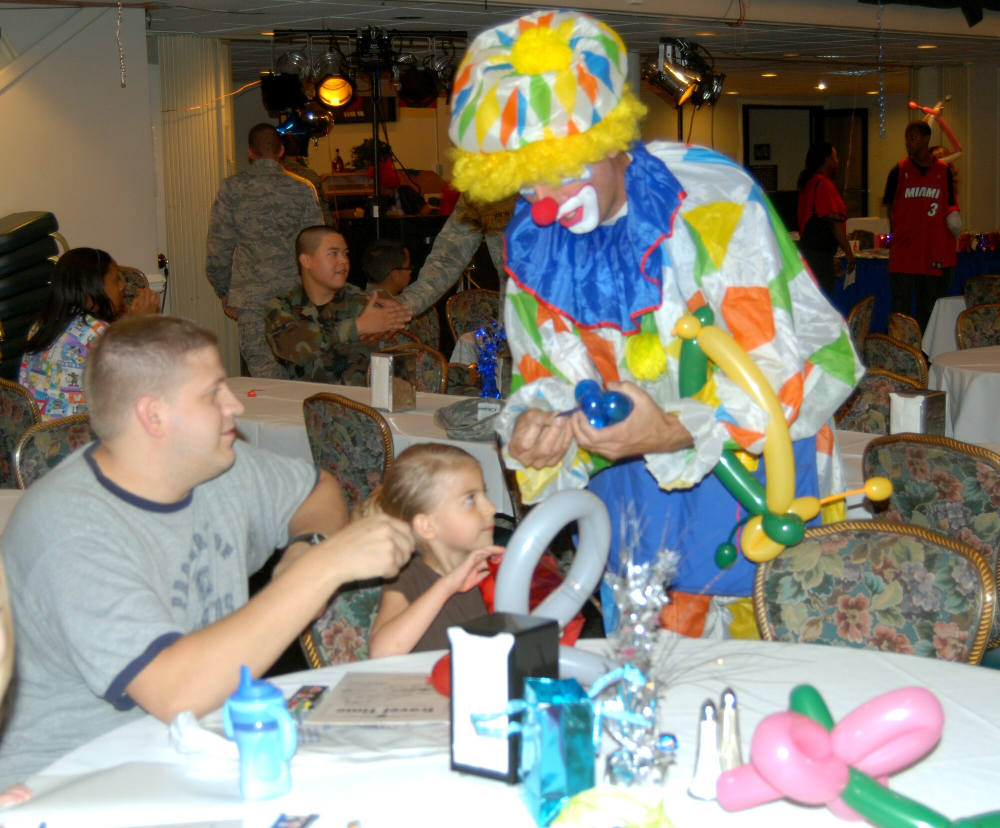 A clown visits a family's table before dinner offering to make balloon hats for everyone. Seeming shy at first, one girl's Dad convinced her to get a hat by letting her pick the colors of her balloons ... and also by getting one for himself. (U.S. Air Force Photo by Emily Smith)