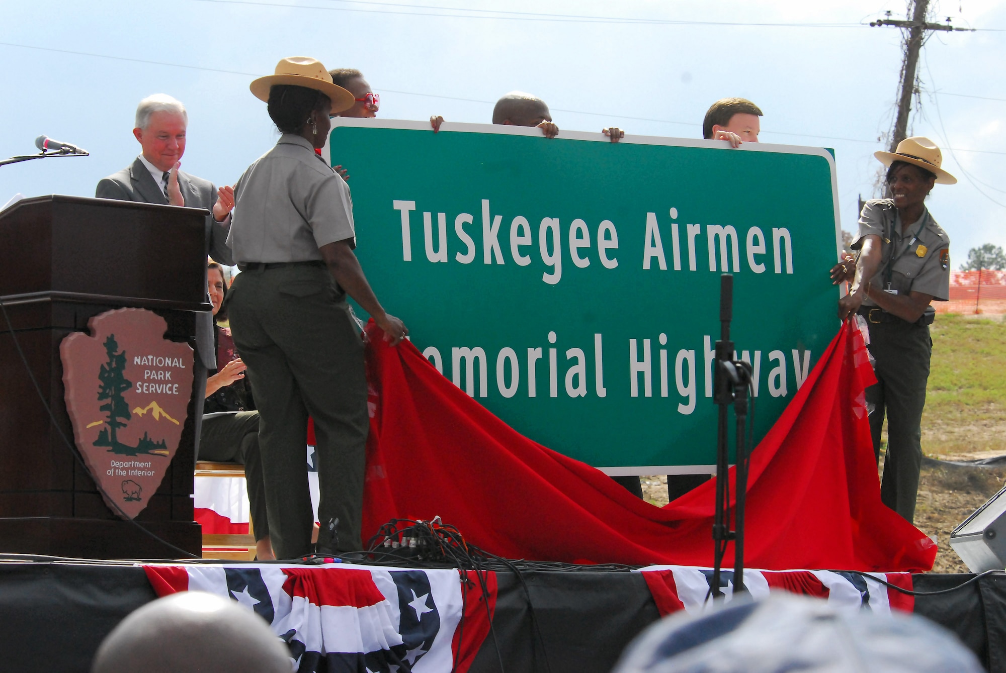 As part of the opening ceremony of the Tuskegee Airmen National Historic Site Oct. 10 at Moton Field, Ala., National Park Service officials unveil a sign that designates part of Interstate 85, which passes near the city of Tuskegee, as the Tuskegee Airmen Memorial Highway. Sen. Jeff Sessions of Alabama looks on from behind. (U.S. Air Force photo/Scott Knuteson)