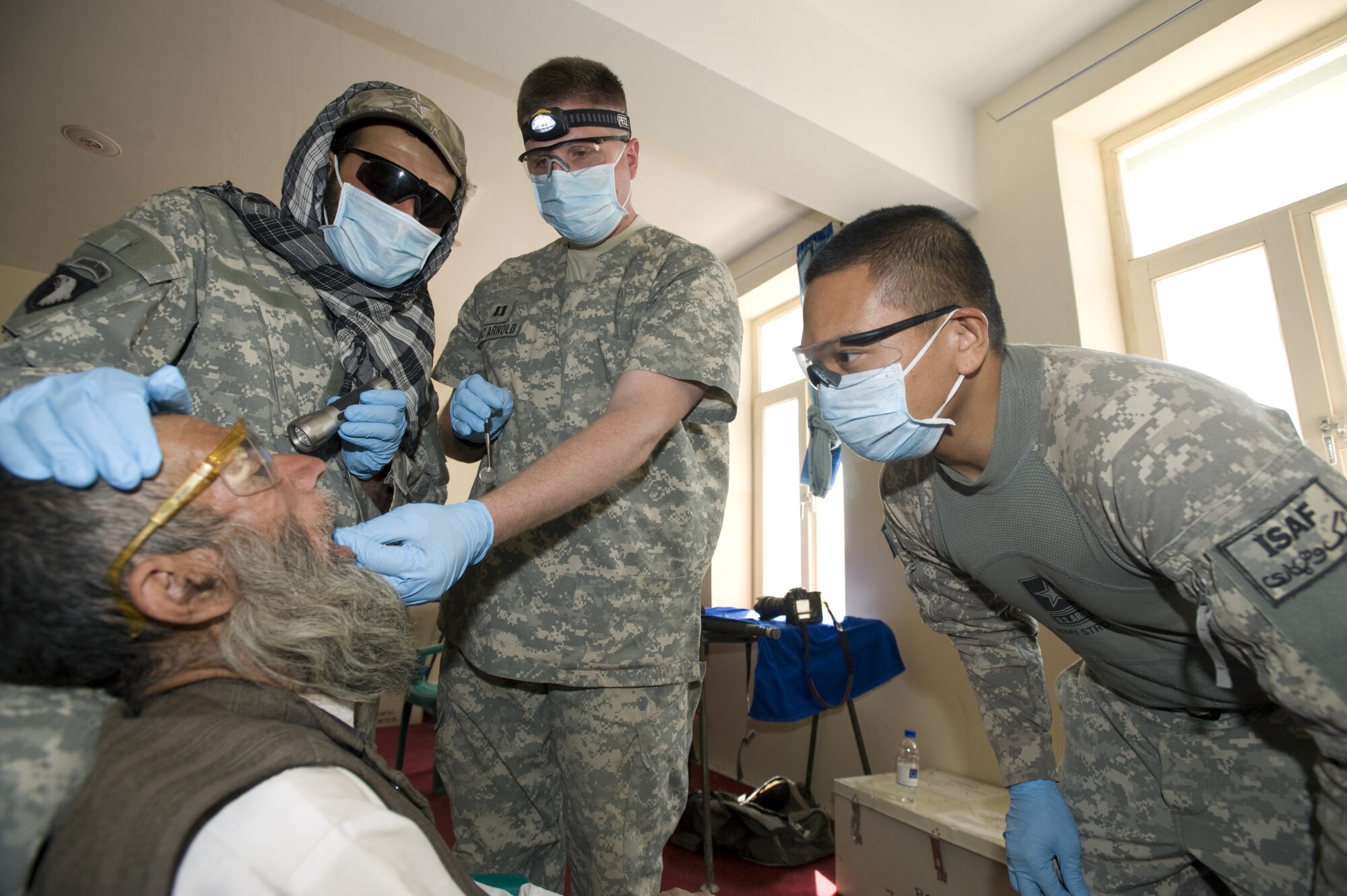 SHAJOY, Afghanistan -- (Left to right) Afghan interpreter John, Capt. (Dr.) James Arnold and Staff Sgt. Nestor Abalos, examine an Afghan man's teeth at a Village Dental Outreach hosted by the Zabul Provincial Reconstruction Team. Although most Afghans lack basic dental hygiene products, their teeth remain relatively healthy due to limited sugar in their diets. When they do have problems many go untreated for years with the lack of basic dental care. The Zabul PRT uses the visits to address these problems, which normally consist of extracting the bad tooth. (U.S. Air Force photo/Master Sgt. Keith Brown)