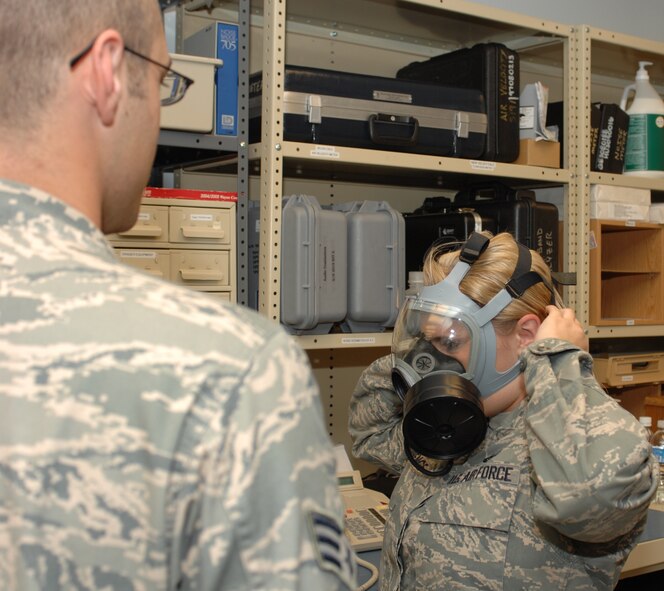 Senior Airman Derek Johnson, 4th Aeromedical Dental Squadron, observes Senior Airman Rebecca Laurence, 4th Logistics Readiness Squadron, as she dons her mask during a gas mask fit test Oct. 9, 2008, on Seymour Johnson Air Force Base, NC. During a fit test, a candle is lit to send particles in the air, which help bioenvironmental technicians detect if the mask has a loose seal. (U.S. Air Force photo by Airman 1st Class Gino Reyes)