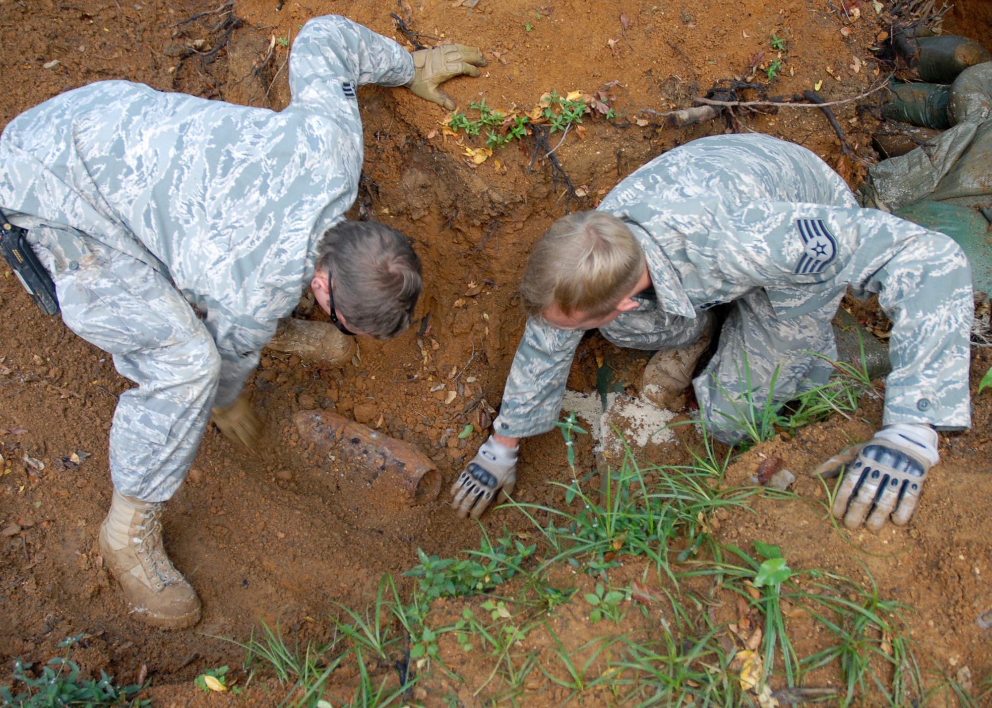 Senior Airman Tristan Persico (left) and Staff Sgt. Jason Weimer (right), 18th Civil Engineer Squadron Explosive Ordnance Disposal specialists, brush away dirt from a UXO at Kadena Air Base, Japan Oct. 19, 2008.  The 18th Wing partnered with local government agencies to successfully remove the UXO while ensuring the safety of local citizens. EOD specialists safely destroyed the munition on the EOD range in the Kadena Munitions Storage Area. The 35-pound World War II-era rocket warheard was discovered near the base fence line during construction activities on Aug. 6. (U.S. Air Force photo/Airman 1st Class Amanda Grabiec)