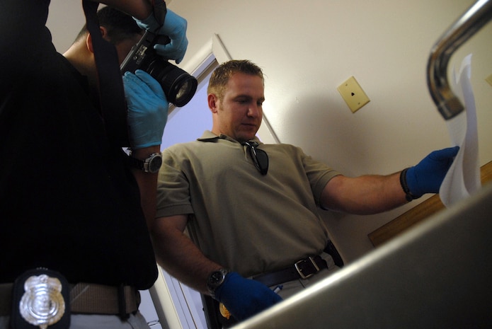 Special Agent Josh Morrison holds open a notebook while Special Agent Jason Akana takes photos during a crime scene investigation exercise in base housing Oct. 17. The Air Force Office of Special Investigations Detachment 310 held the exercise simulating a suicide to test their CSI skills. The suicide note was written in the notebook. Agents Morrison and Akana are assigned to AFOSI Det. 310. (U.S. Air Force photo/Staff Sgt. Sam Hymas)

