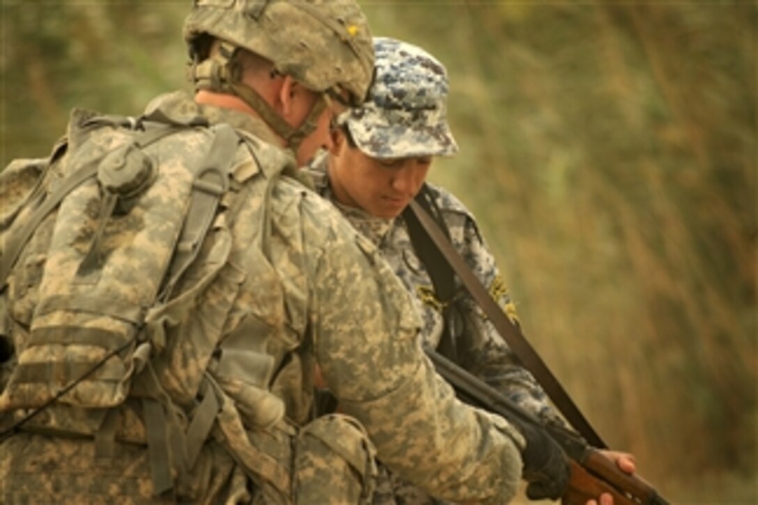 A U.S. Army soldier attached to the 4th Infantry Division shows an Iraqi soldier weapon-handling techniques during a patrol in Abu T'Shir, Iraq, on Oct. 16, 2008.  
