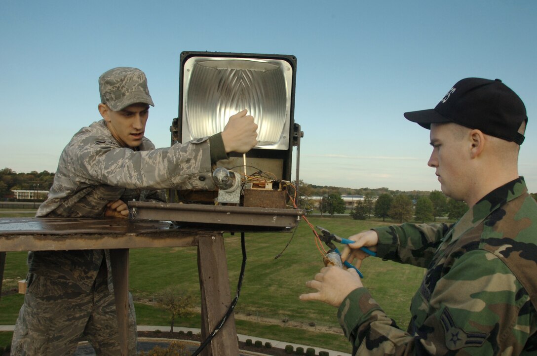 316th Civil Engineer Squadron electrical systems apprentices, Airman 1st Class Benjamin Floyd, left, and Airman 1st Class David Posey change out an old ballast on a 400 watt high pressure sodium perimeter light at the south corner atop  the 316th Wing Headquadrters buillding 1535 Tuesday. (U.S. Air Force photo by Bobby Jones)
