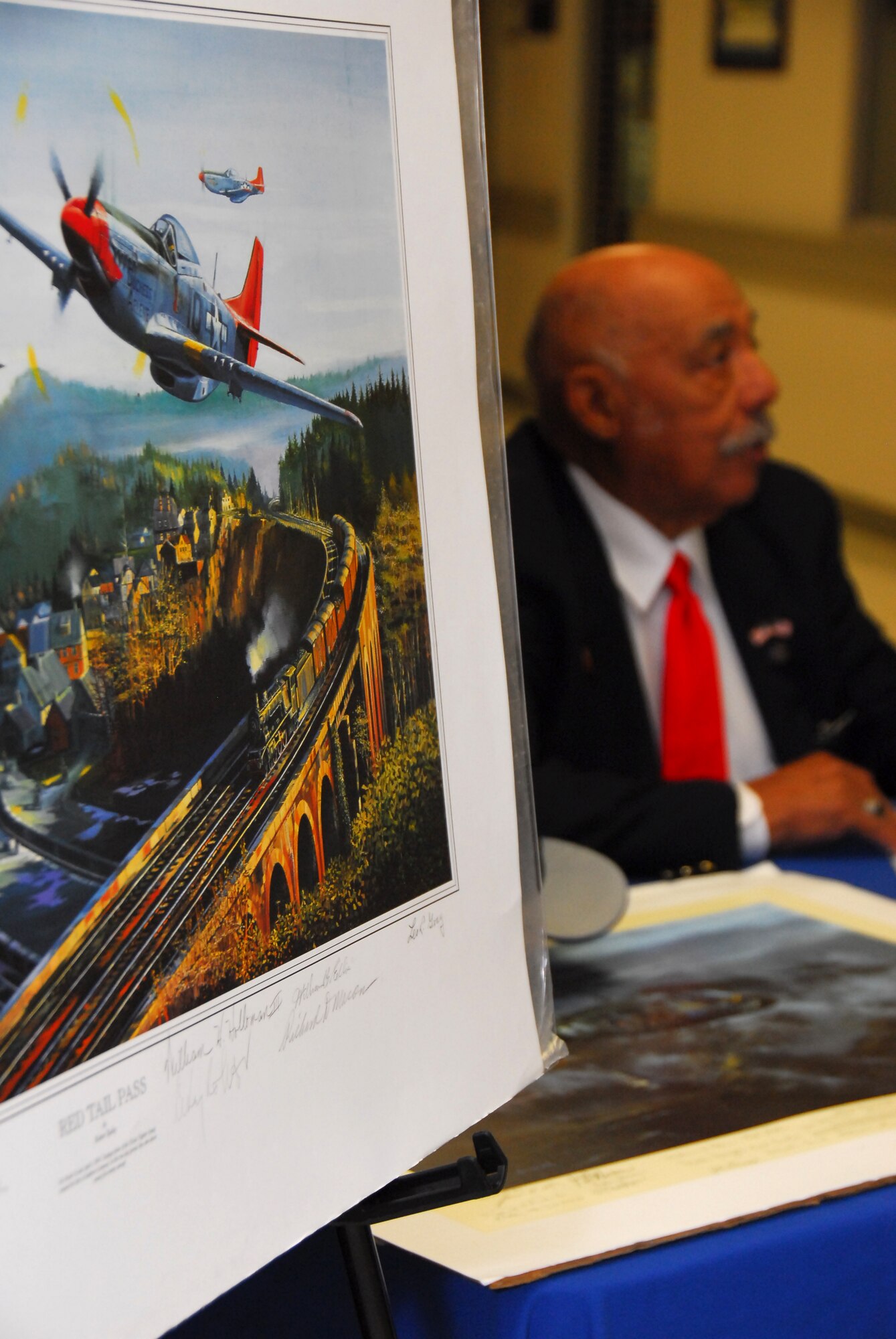 Retired Lt. Col. William Holloman, one of the original Tuskegee Airmen, signs autographs near a lithograph depicting the Tuskegee Airmen in combat during World War II. (Air Force photo by Scoot Knuteson)