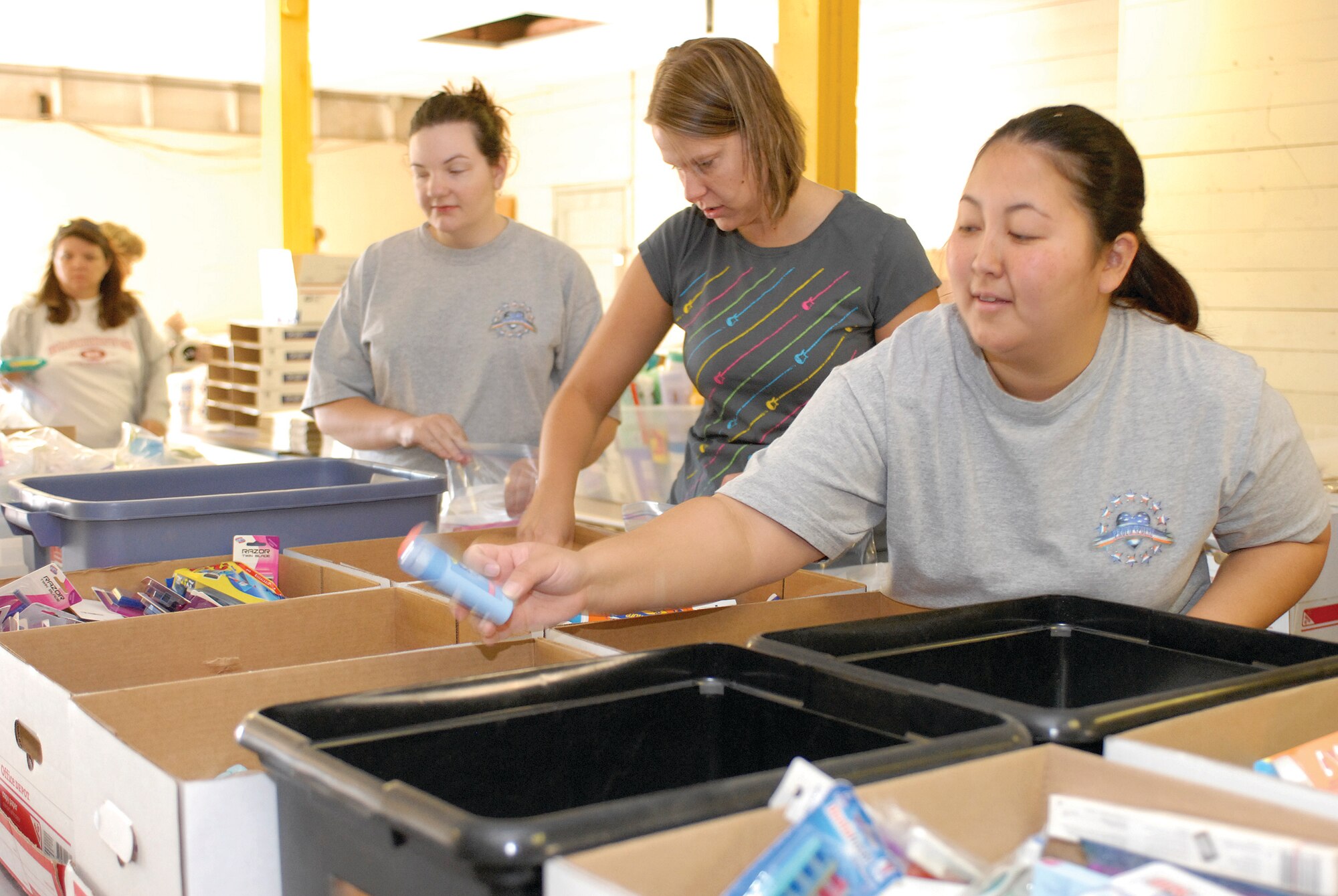 FROM LEFT: Patricia Beighle, Luke Enlisted Spouses Club president, and members, Molly Gazzo and Sara Souza, help pack boxes that will be shipped off to deployed Luke members as part of Operation Thunderbox. Toiletries, food and a varitety of other items were donated from local businesses, and members of the ESC volunteered their time to help put the boxes together. (U.S. Air Force Photo/Deborah Silliman-Wolfe.)