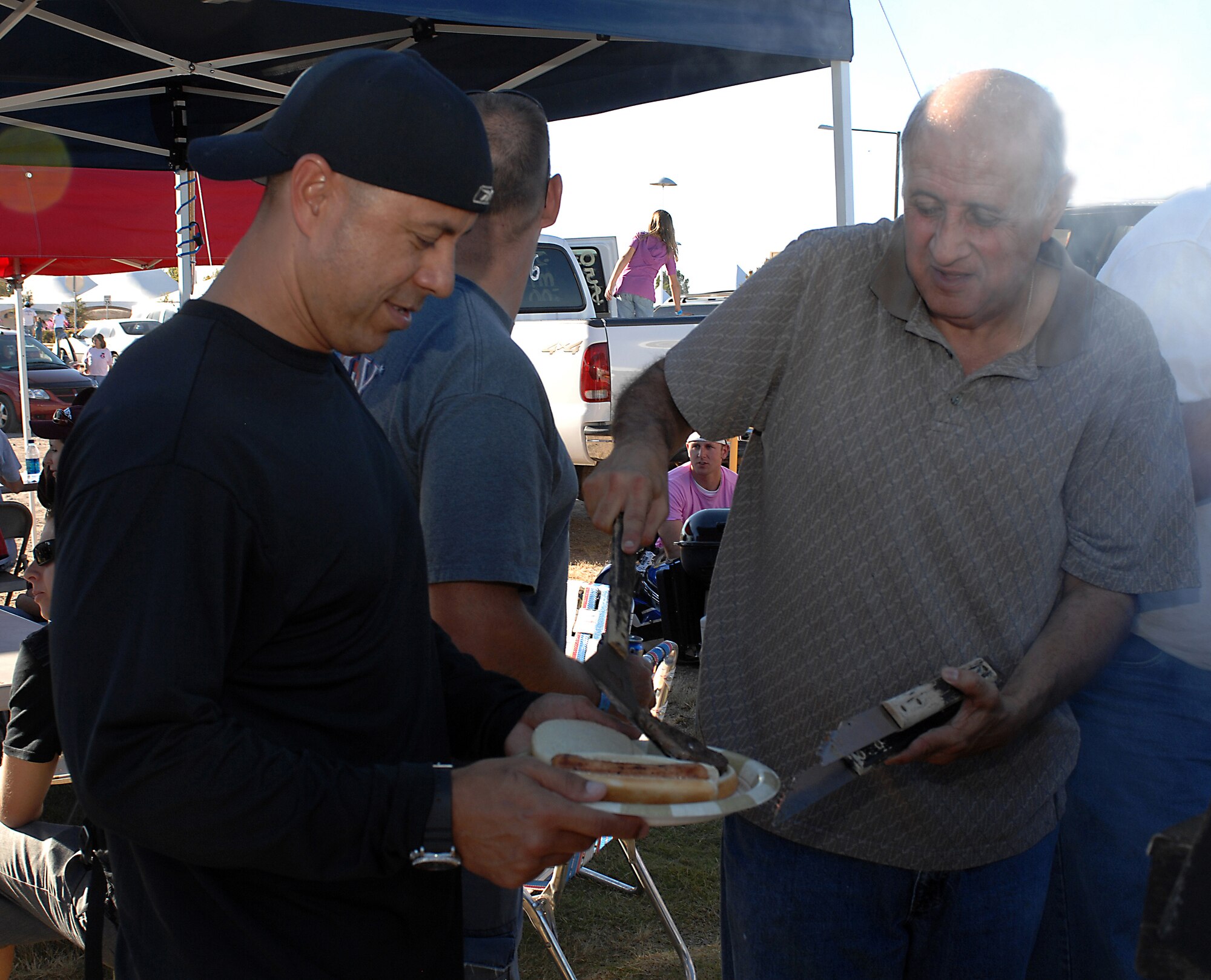 Juan Mejia, 49th Operations Group secretary, serves a burger to Chief Master Sgt. Jeffery Cui, 49th Fighter Wing command chief, during the tailgate party hosted by the 49 OG from Holloman Air Force Base, N.M., before the New Mexico State University game against San Jose State at NMSU, October 18. More than 80 Team Holloman Airmen, family and friends attended the party. (U.S. Air Force photo illustration/Airman Sondra M. Escutia)