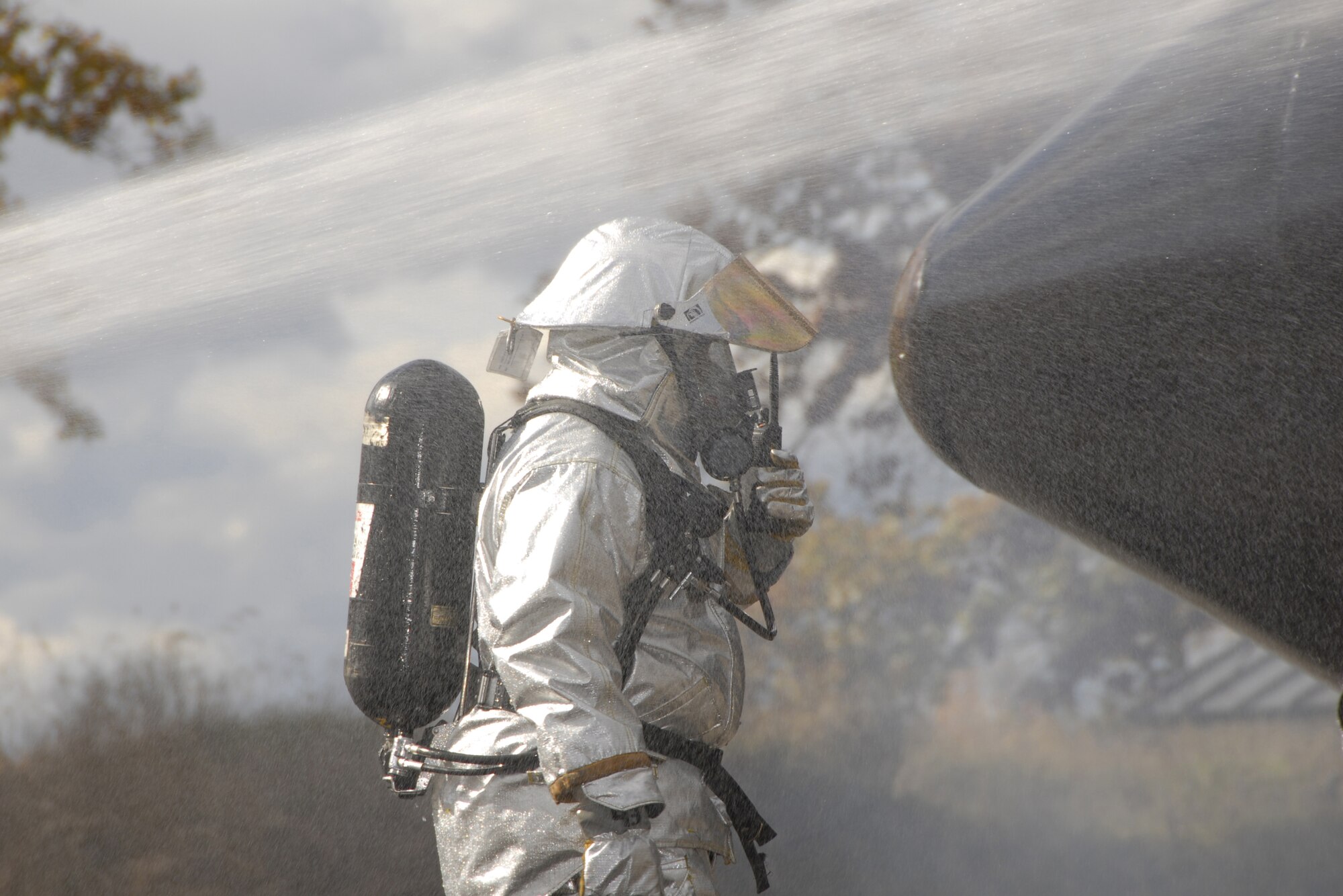 A Rescue Crew Chief of the 127th Fire Department, Selfridge ANGB, Mich., walks under the stream of a charged fire hose while communicating to rescue team members via radio during a simulated aircraft crash site drill Oct. 18 at the CRTC training base in Alpena, Mich. The Rescue Crew Chief’s job is to safely enter a potentially volatile area and locate survivors or fatalities.  (U.S. Air Force photo by Tecnical Sgt David S. Kujawa)