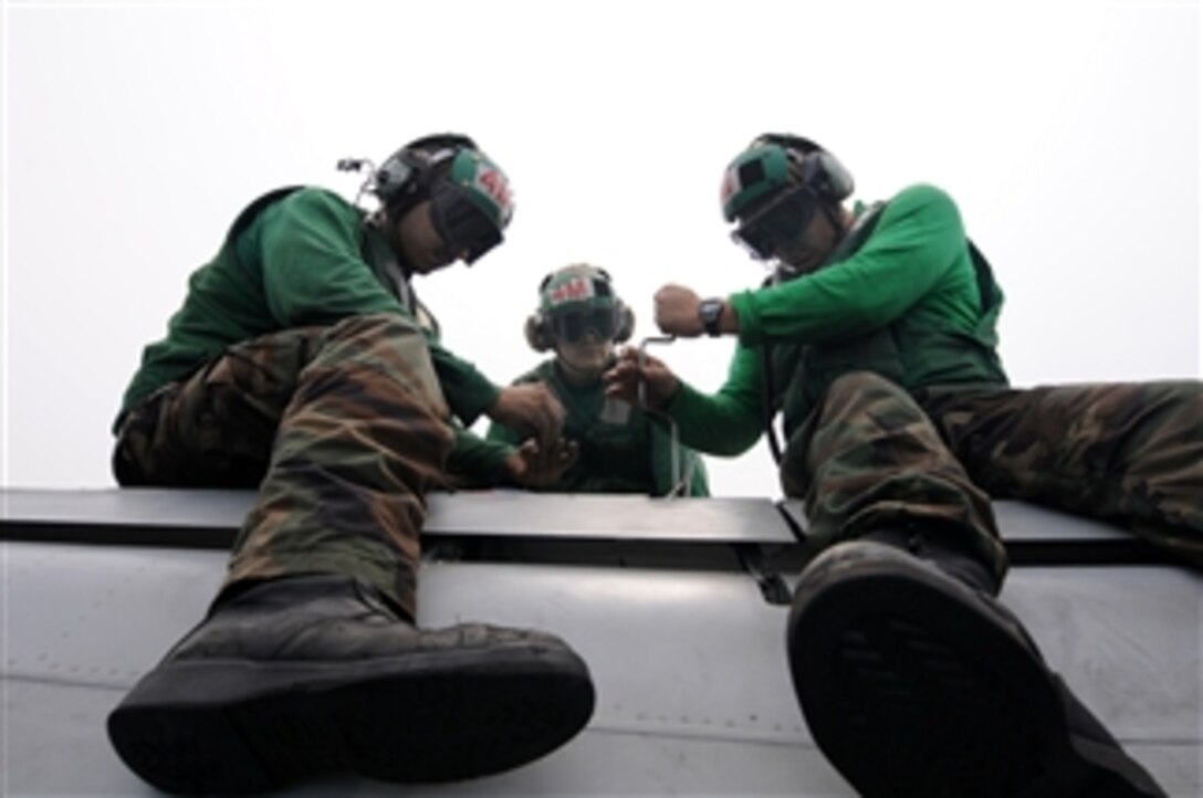 U.S. Navy Petty Officer 2nd Class Andrew Miller uses a speed handle to replace screws on a panel as Petty Officer 2nd Class Jesus Andrade (left) and Petty Officer 3rd Class Omar Yacsavilca watch on the flight deck of the aircraft carrier USS Ronald Reagan (CVN 76) while underway in the Indian Ocean on Oct. 21, 2008.  The sailors are all assigned to Strike Fighter Squadron 25.  The Ronald Reagan Carrier Strike Group is participating in exercise Malabar '08, which is designed to increase cooperation between the Indian navy and U.S. Navy while enhancing the cooperative security relationship between India and the United States.  