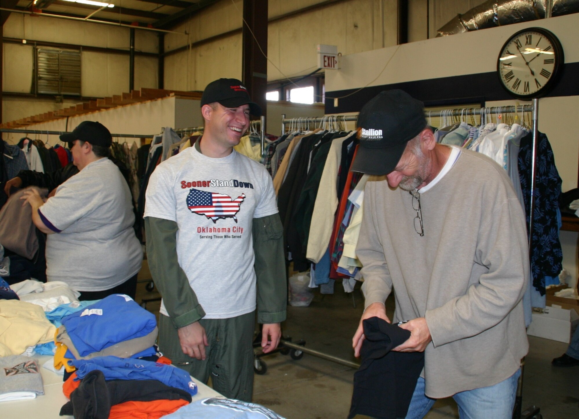 Senior Airman Jesse Parisot, 964th Airborne Air Control Squadron, shares a laugh with a veteran as they find clothes to fill his backpack. Photo Courtesy of 1Lt Kinder Blacke.