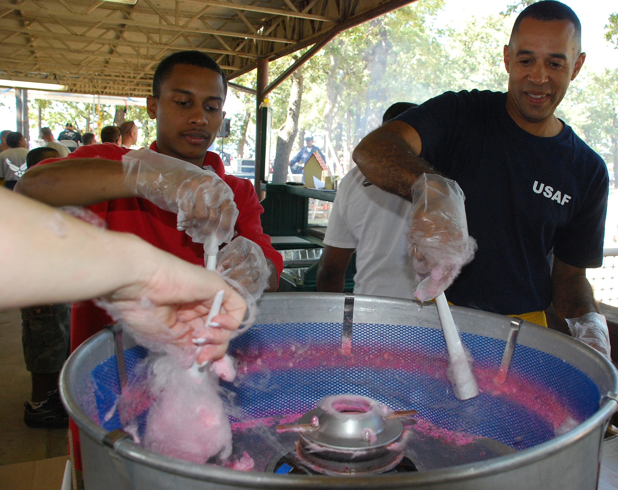 Lt. Col. Bradford Montgomery, 301st Mission Support Group executive officer, and Senior Airman James Stirgus, 301st Communications Flight client support administrator, practice their cotton candy-making technique. Hundreds of 301st Fighter Wing Airmen and their families gathered for the annual picnic. This year's food service donned a different aire with more of a carnival atmosphere. Food, cooked by various squadron members, included  corn dogs, hamburgers, fried pies, turkey legs, and of course fried brownie bites. (U.S. Air Force Photo/Tech. Sgt. Julie Briden-Garcia)
